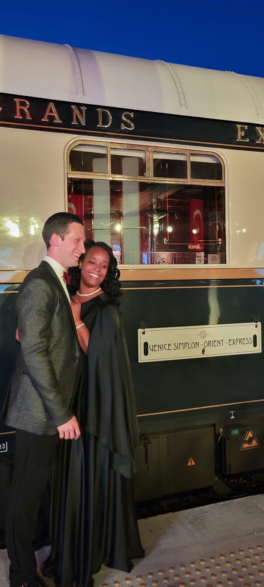 A couple posing outside of a restaurant in the evening.