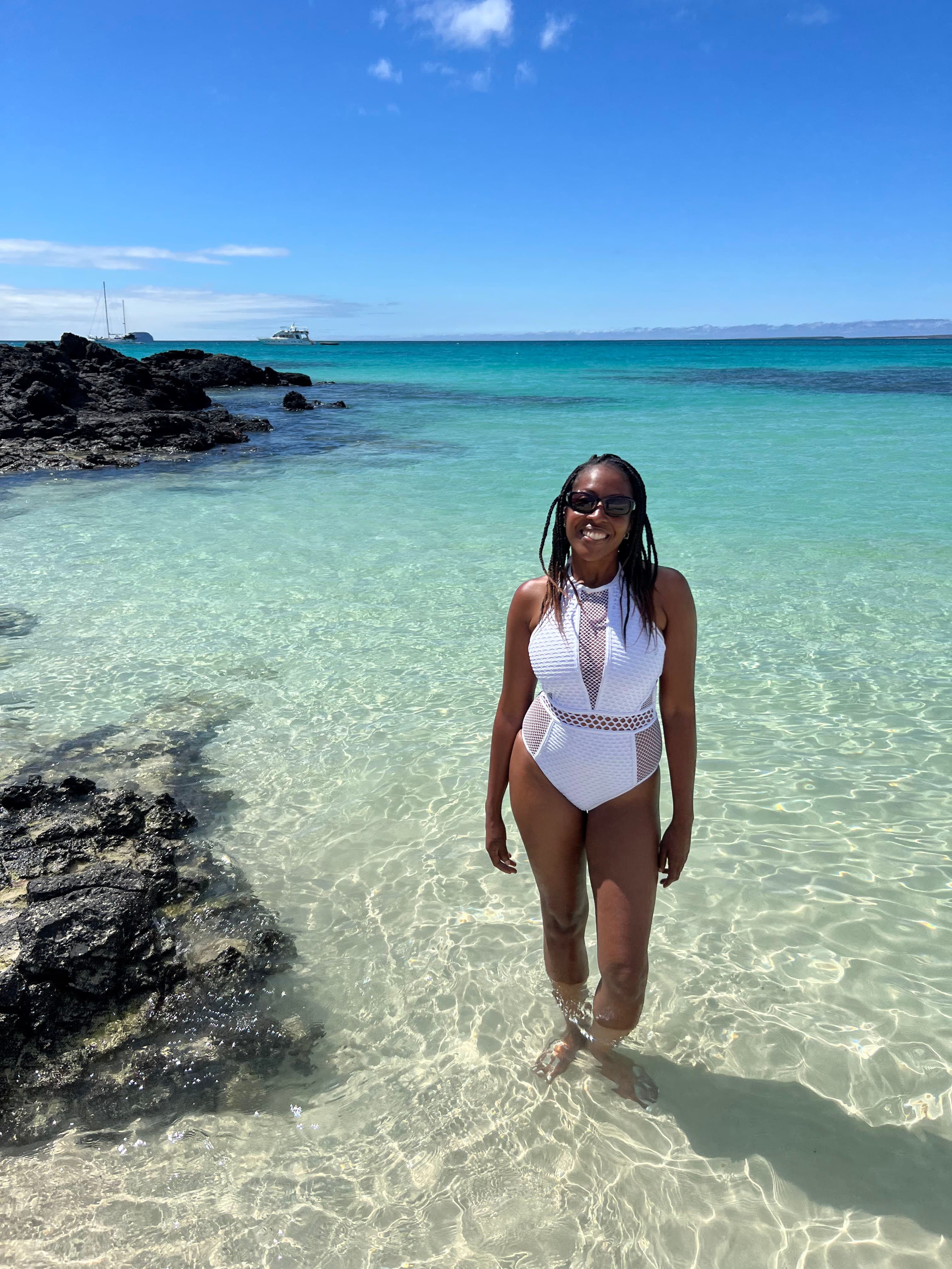 Advisor posing on a sandy beach as waves gently lap the shore on a sunny day.