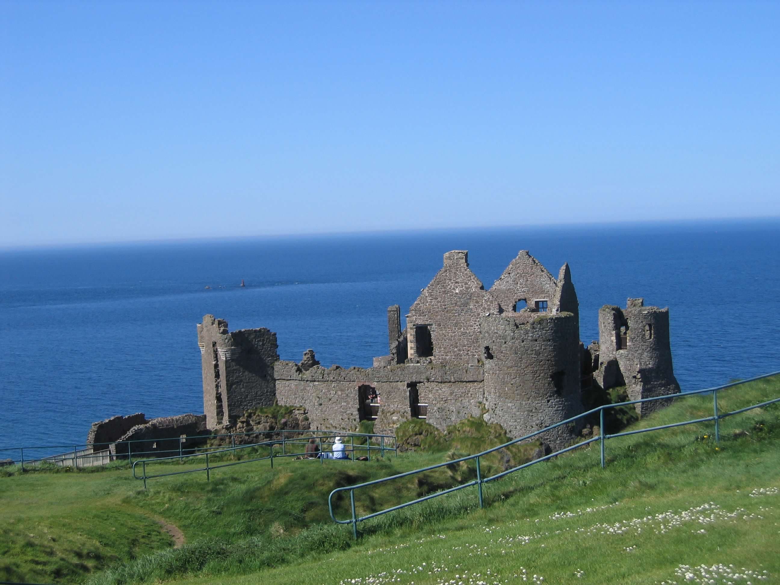 A view of a castle on a sunny day with the ocean in the distance.
