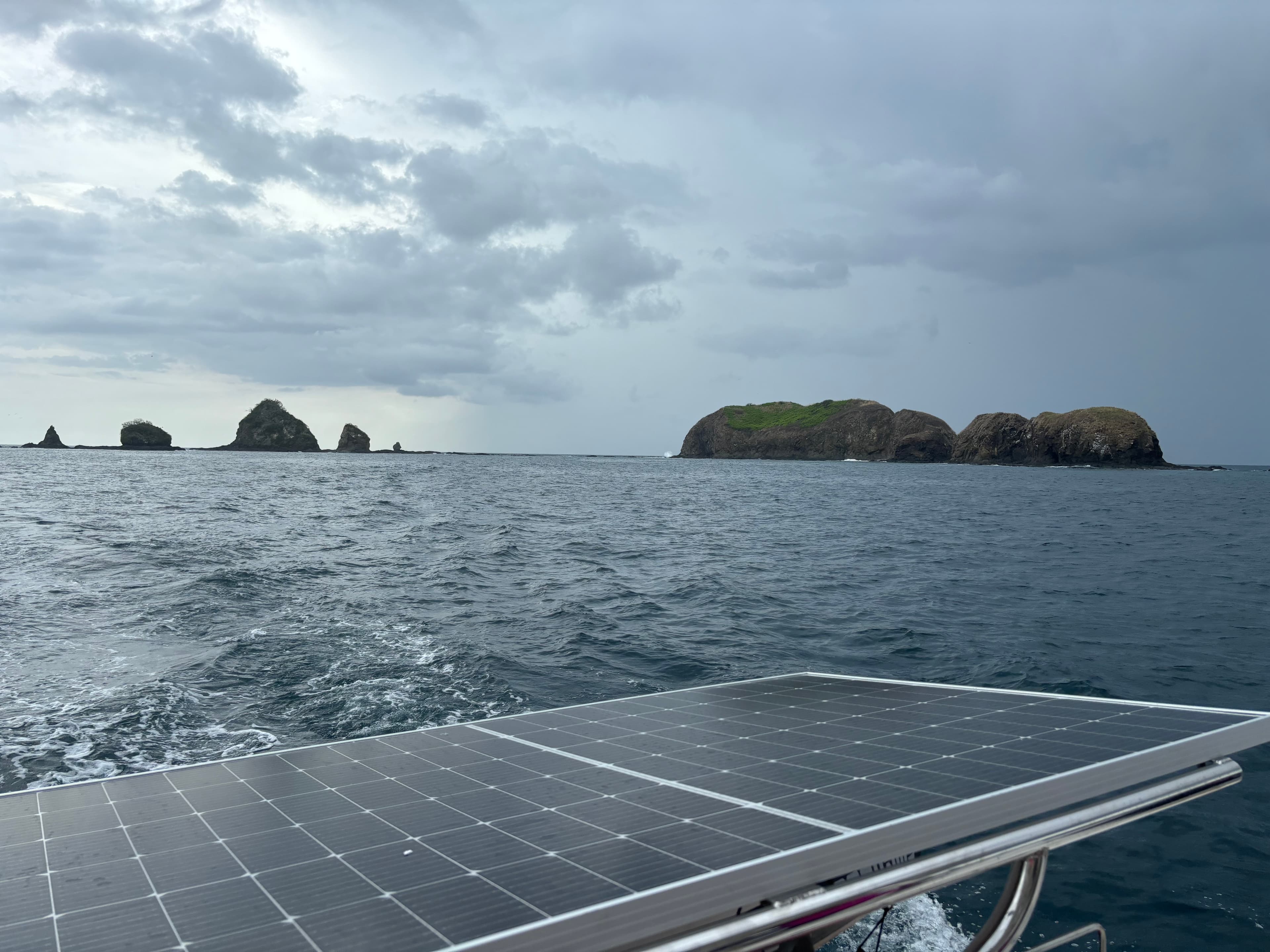 View of a solar panel and the sea with rock formations in the distance under cloudy skies