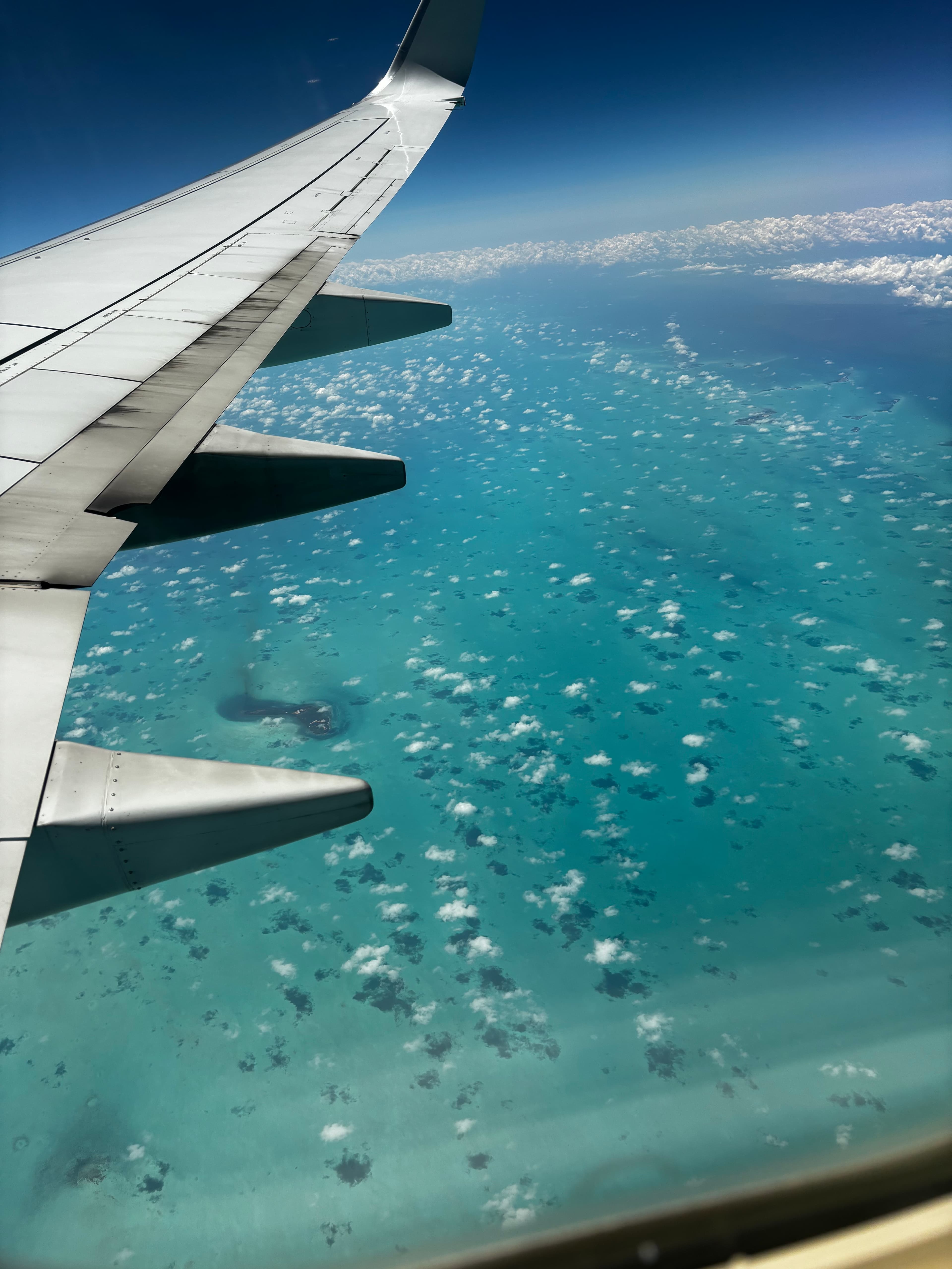 View of small clouds floating above a turquoise sea as seen from a plane window