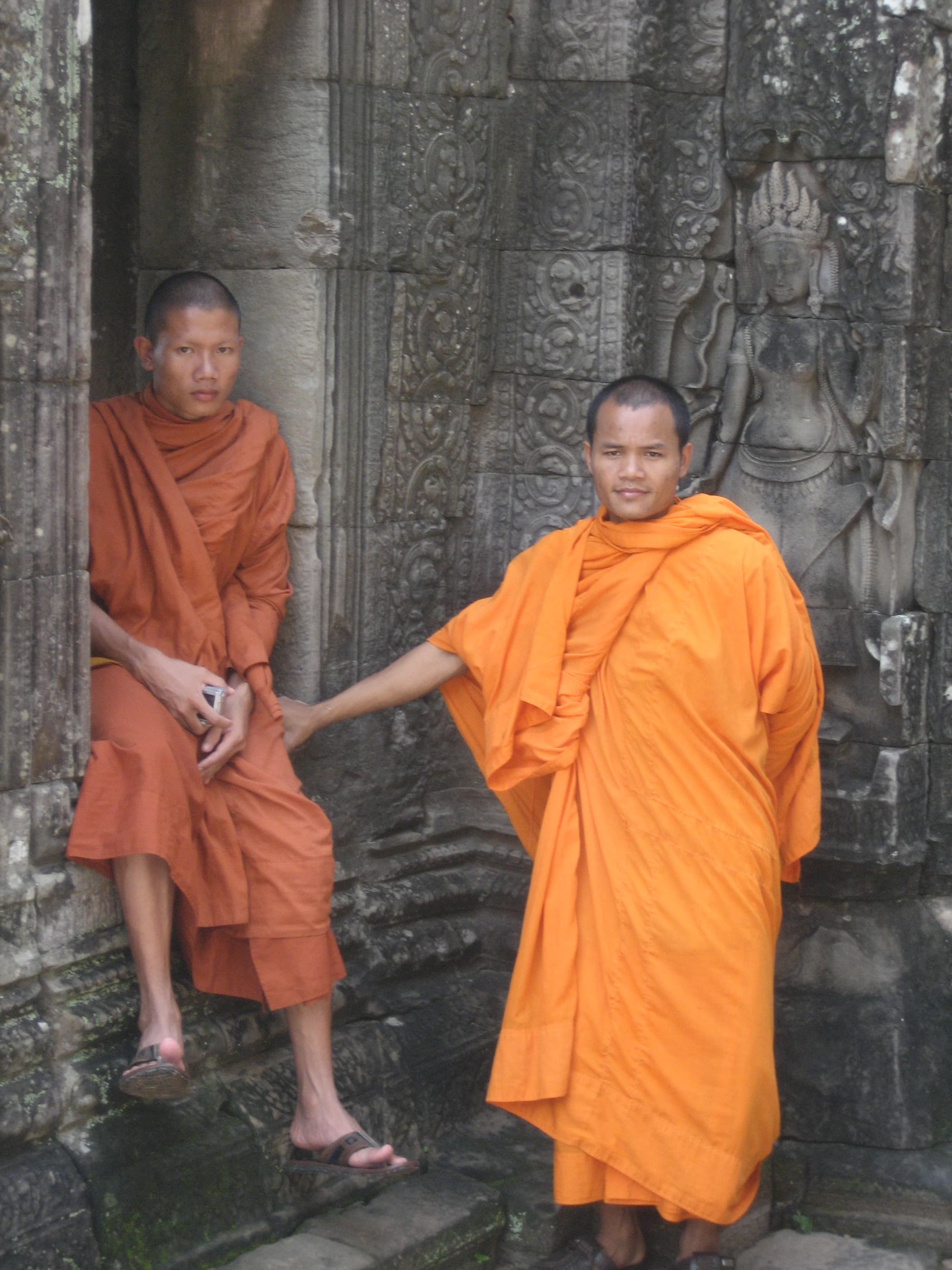 Two monks in orange robes sitting on a stone wall