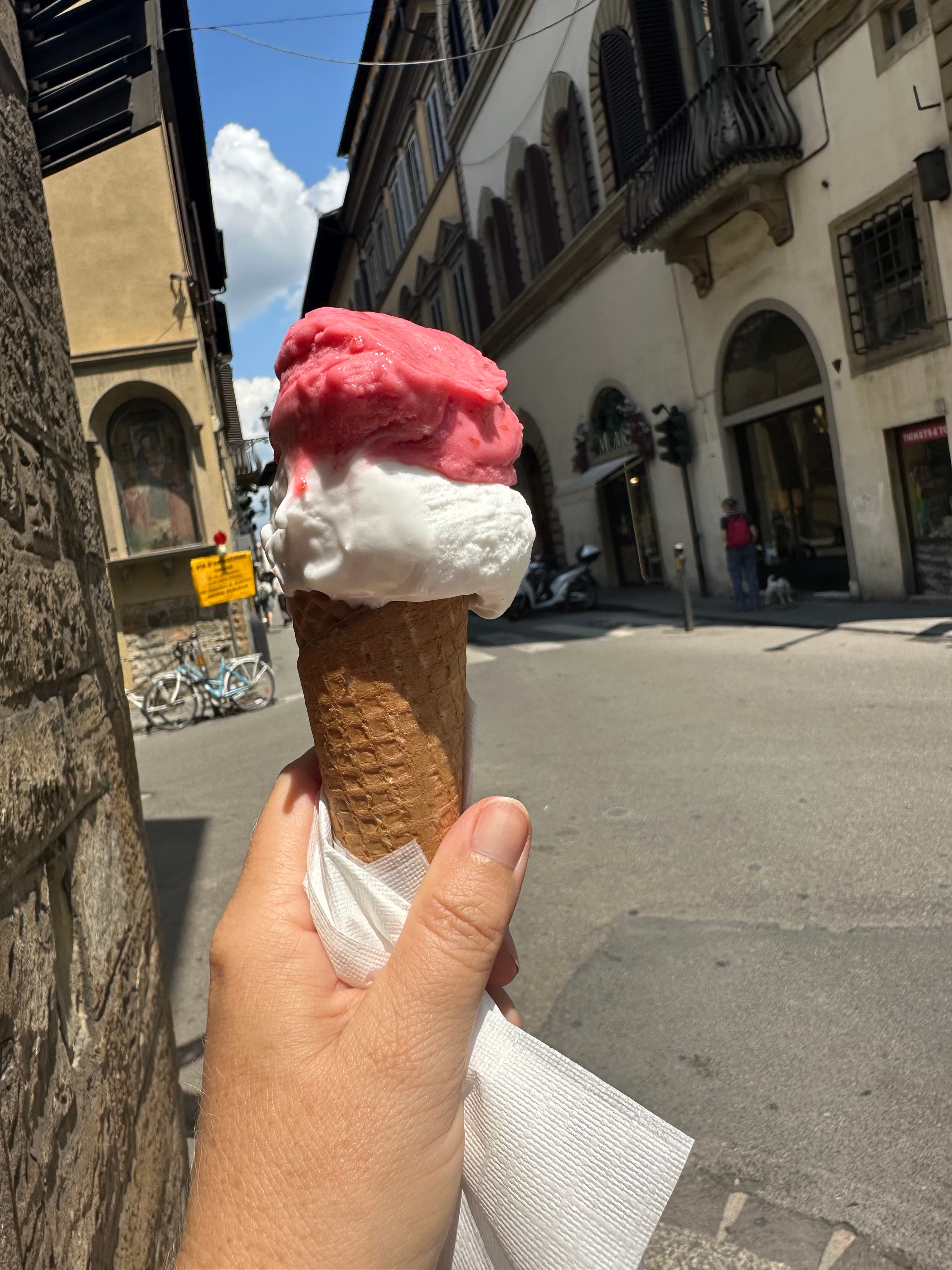 A hand grips an ice cream cone featuring pink and white ice cream.