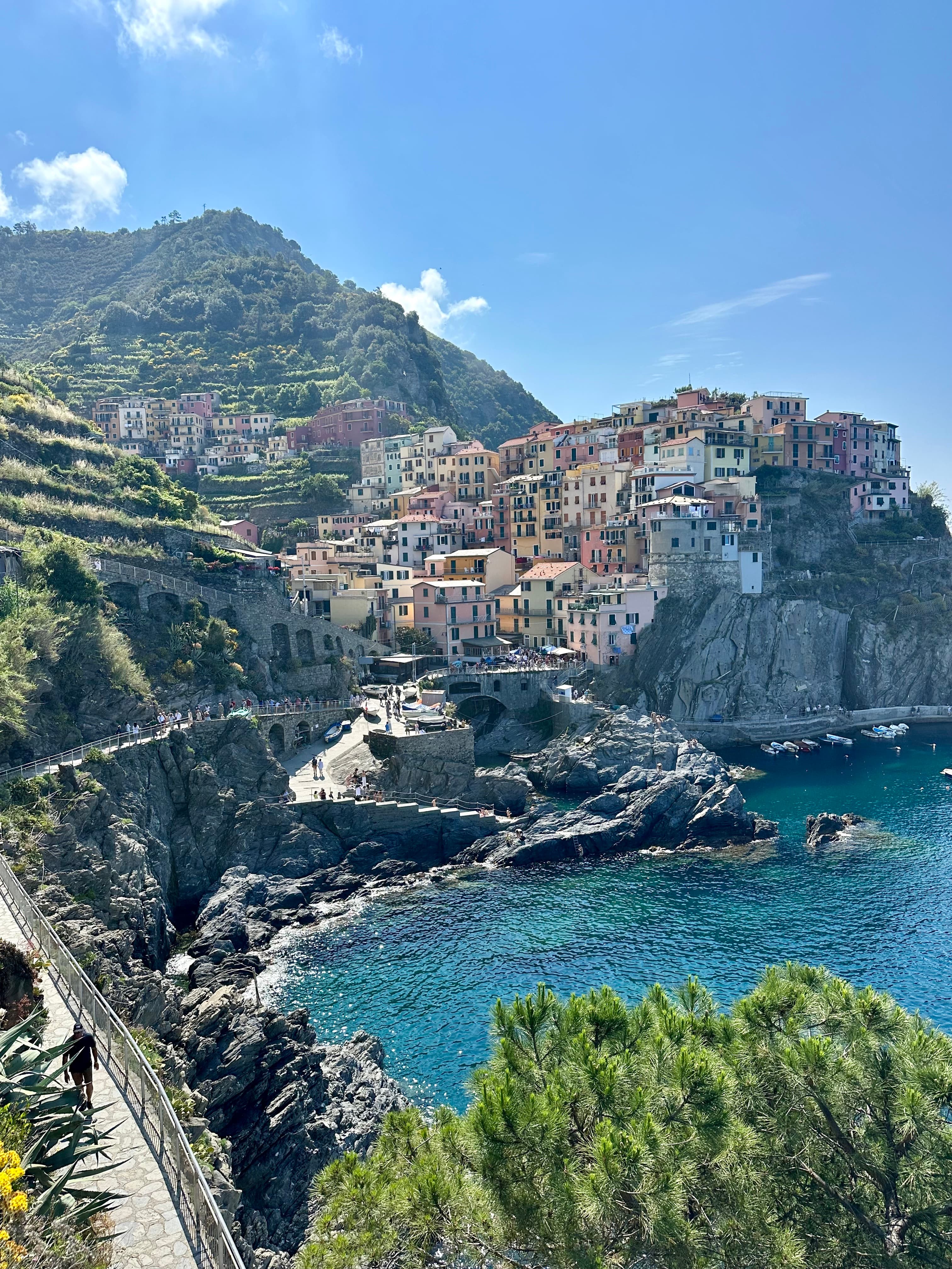 A scenic pathway leading to the picturesque village of Manarola, Italy, surrounded by lush greenery and coastal views.
