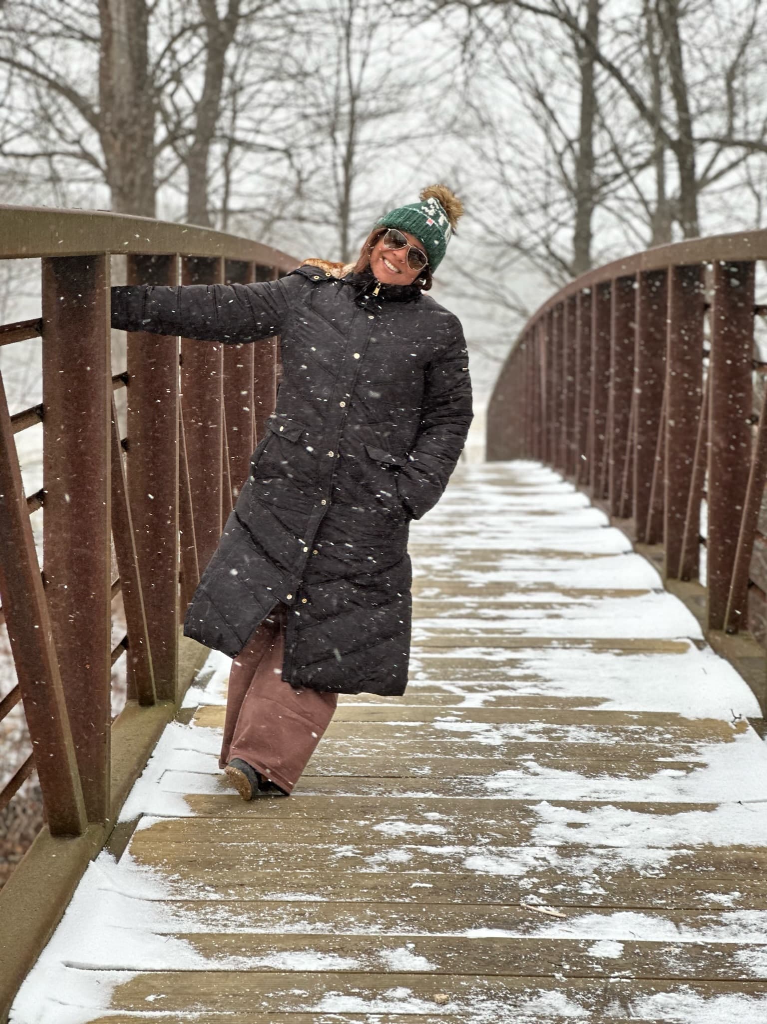 Advisor in a winter coat and puffy hat posing on a narrow wooden bridge in the snow