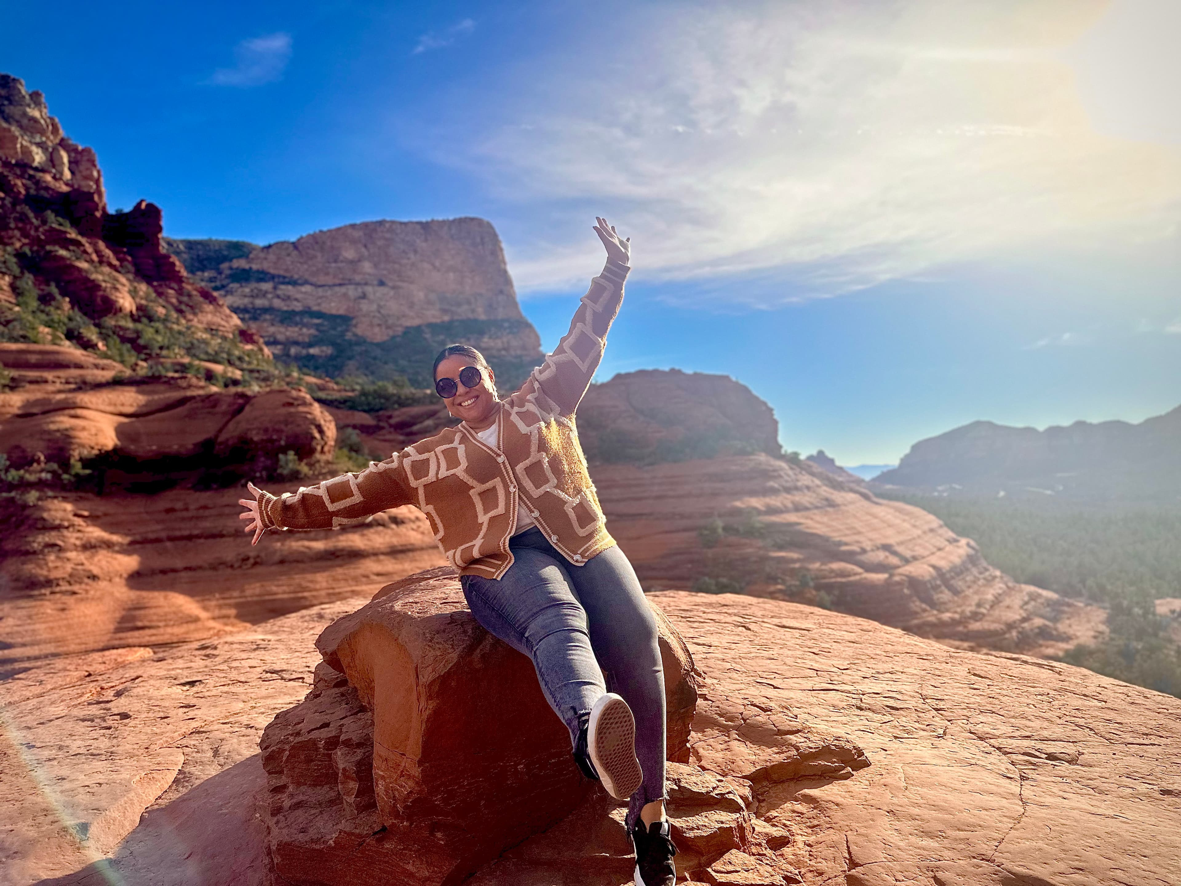 Advisor sitting on a red rock with arms raised overlooking a beautiful canyon