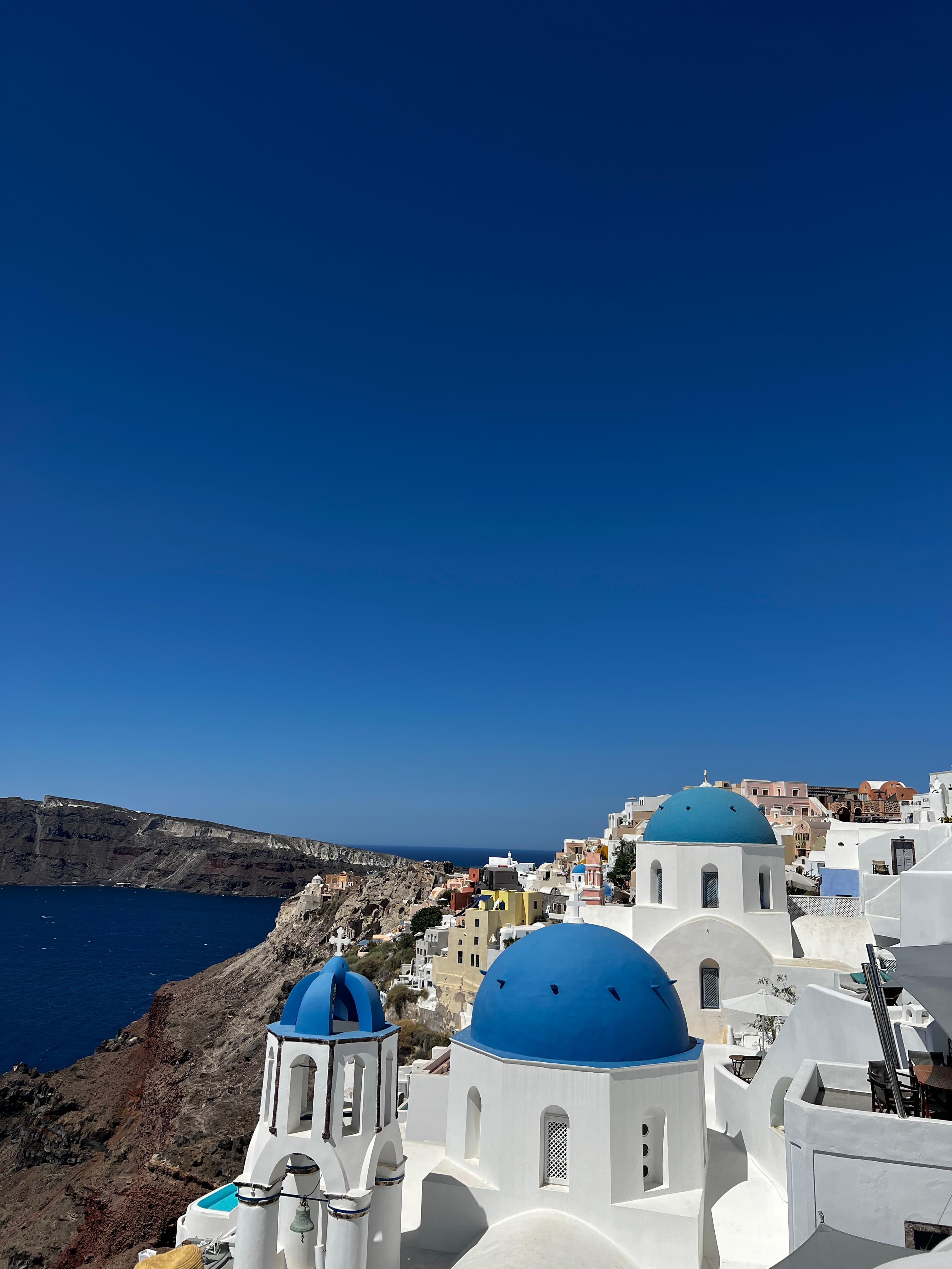 Beautiful view of white buildings with blue domed rooftops on seaside cliffs under clear skies