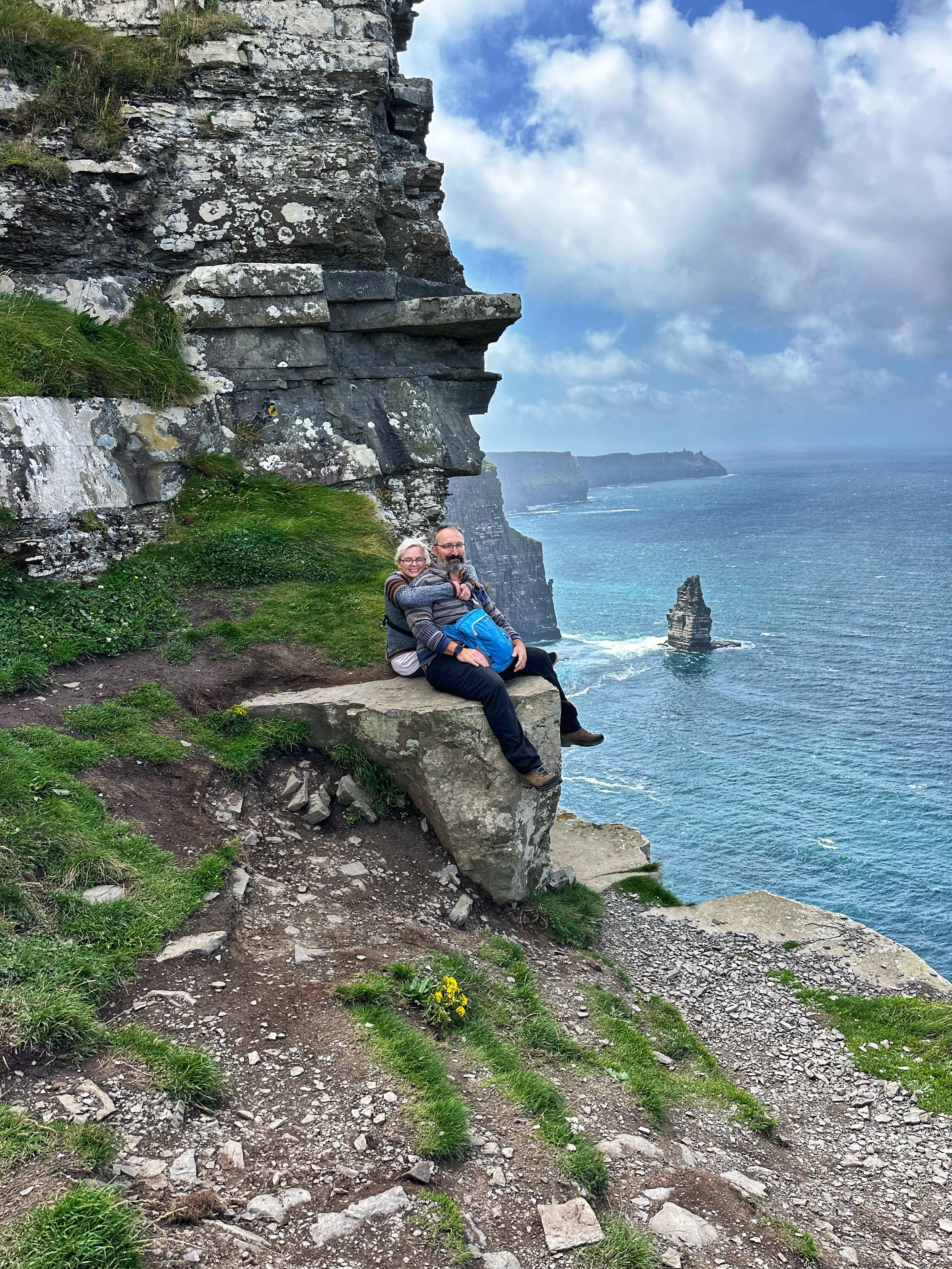 View of two people sitting on a rock overlooking a beautiful dramatic coastline