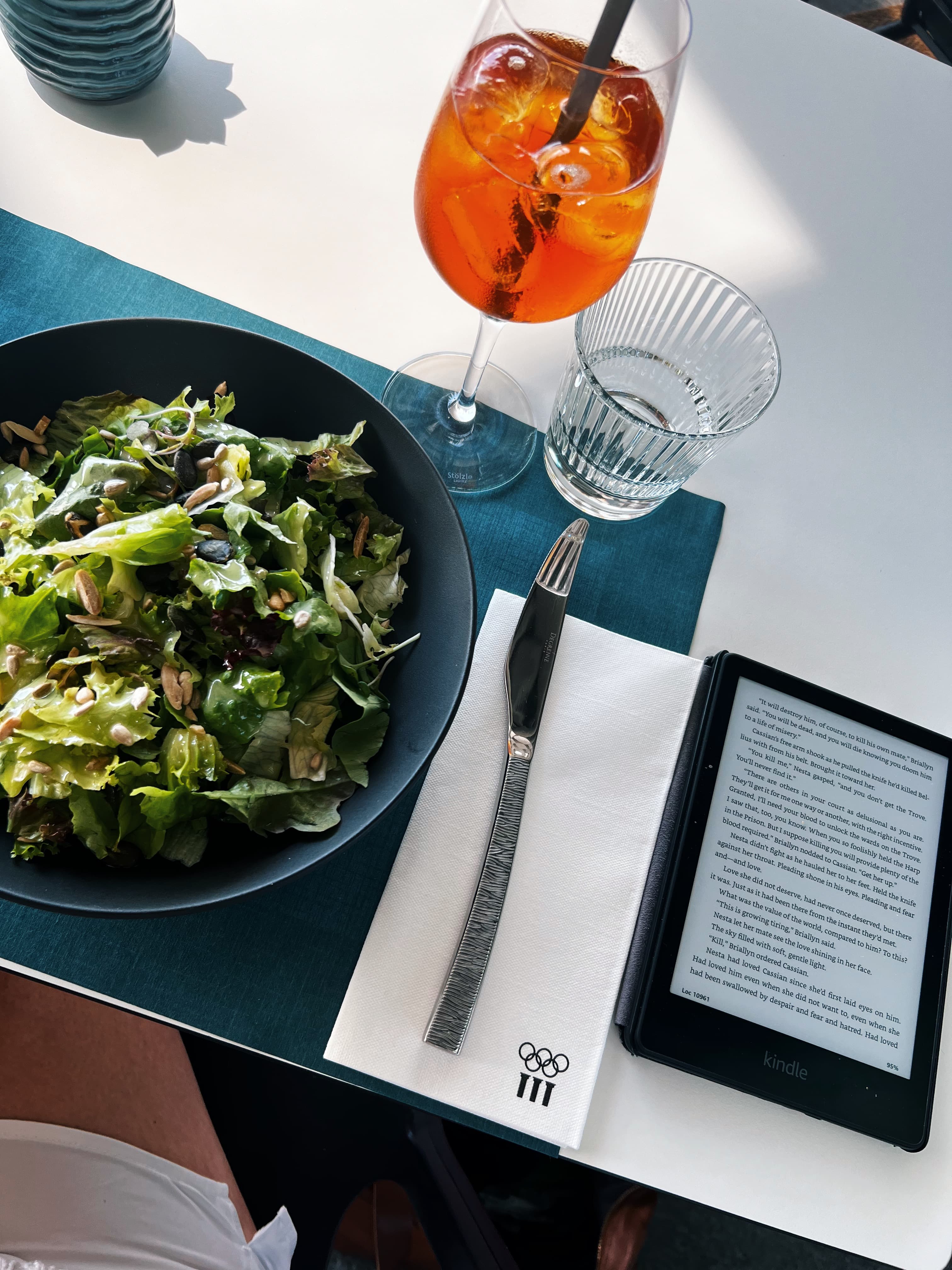 View of a salad and Aperol Spritz beside an e-reader on a white restaurant table