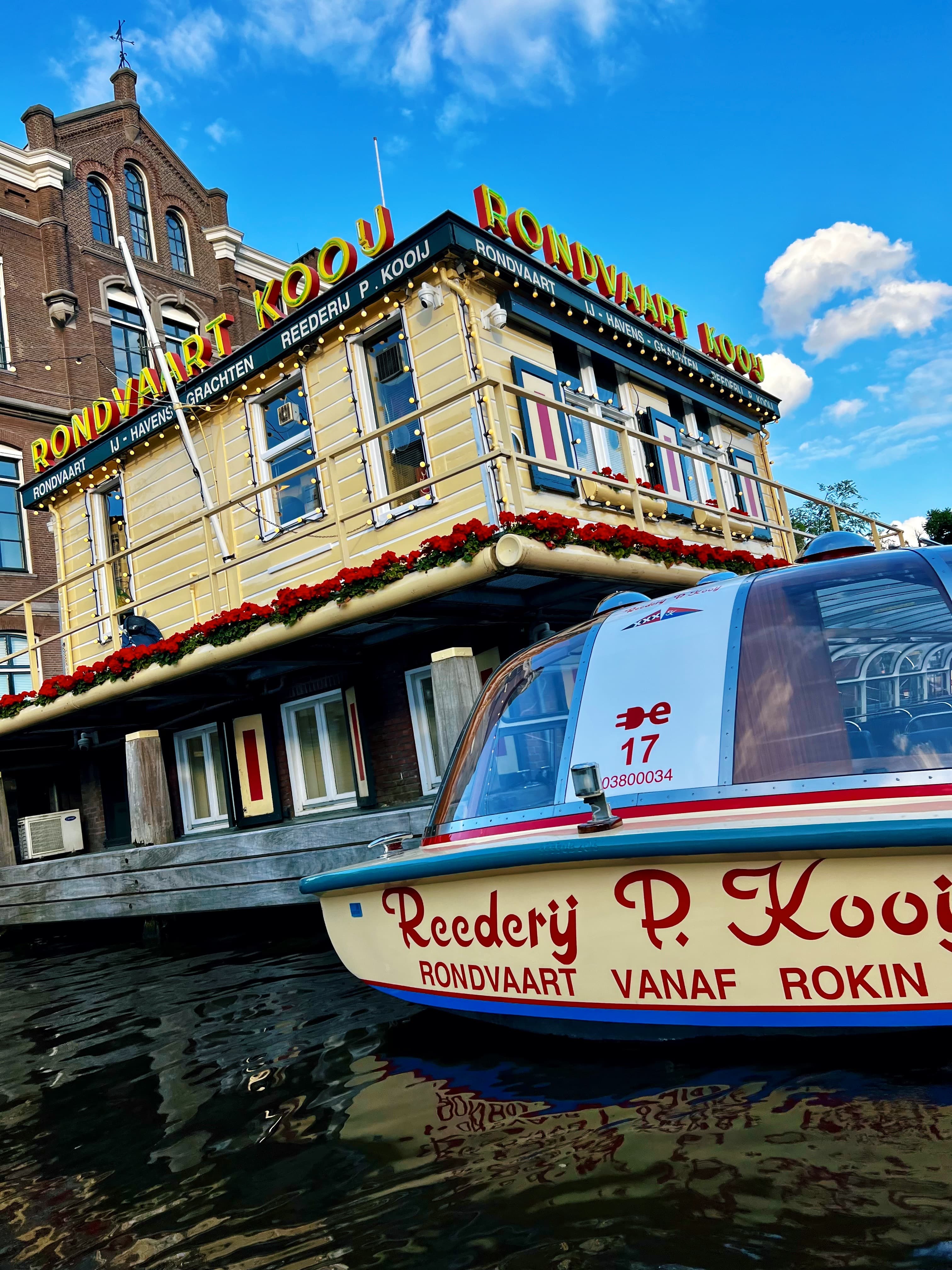 View of a yellow boat and building with red flowers by a canal on a sunny day