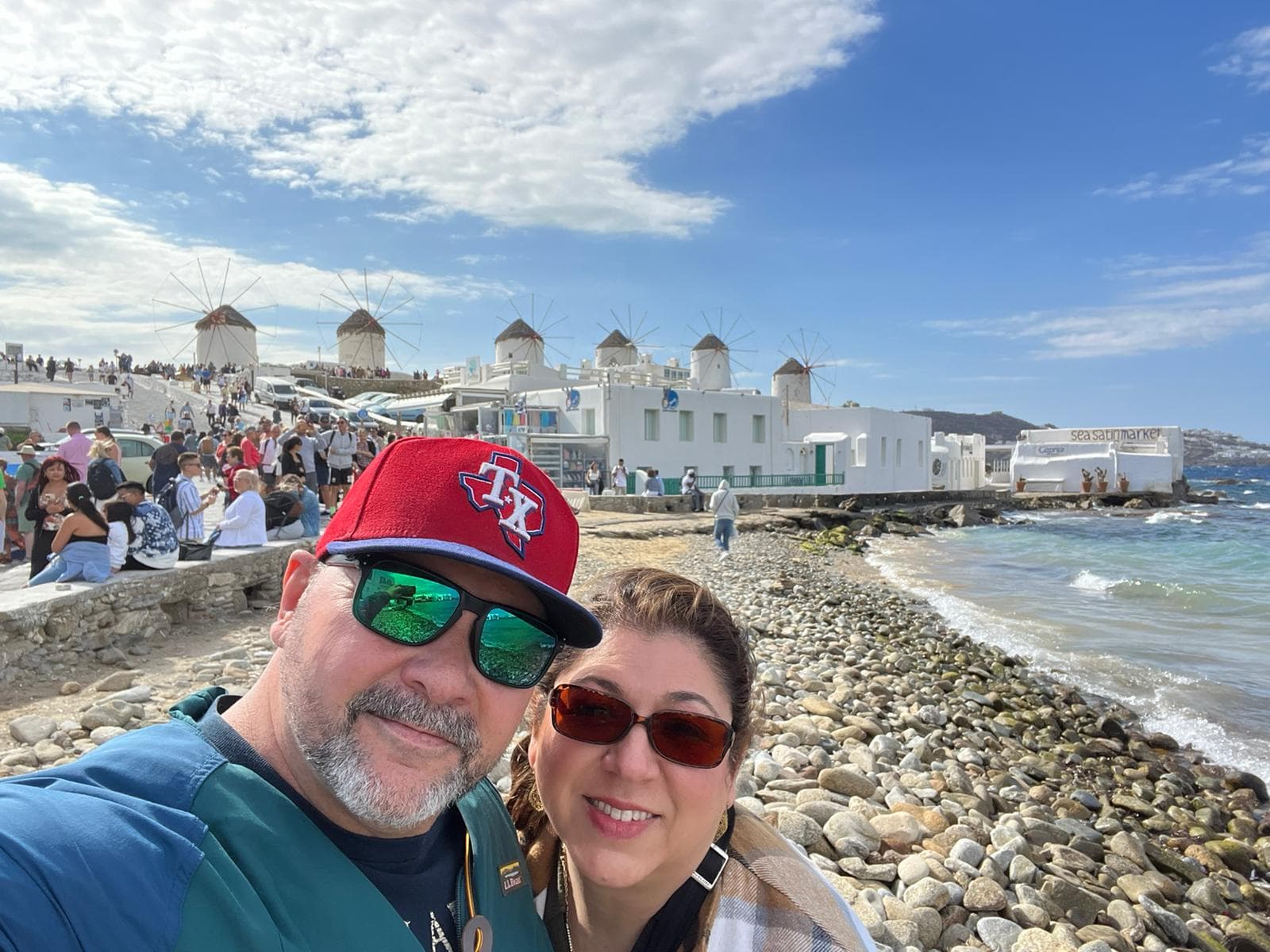 A couple enjoying a beach day, posing for a selfie with the ocean waves and sandy shore in the background.