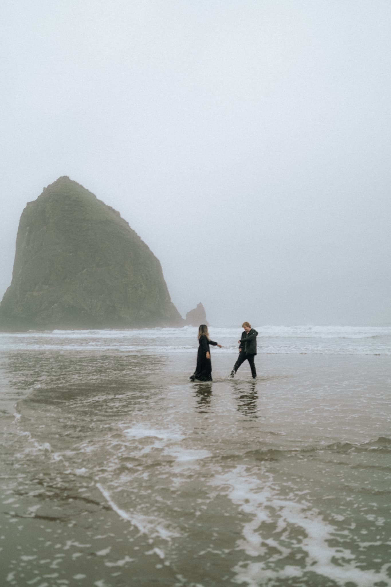 A couple poses on Cannon Beach, Oregon, with the iconic Haystack Rock in the background.