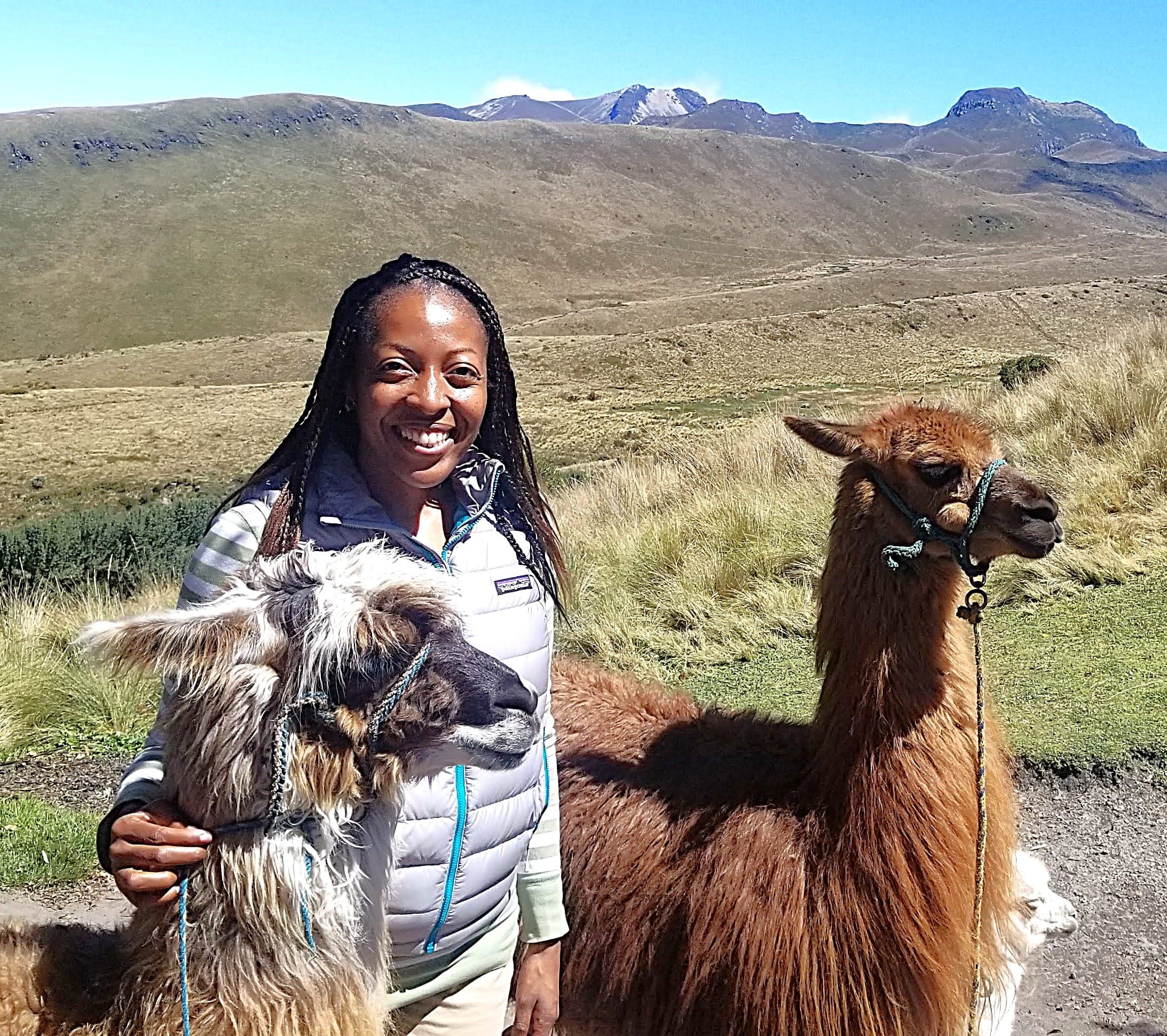 Advisor posing in between two llamas with a mountain background on a sunny day