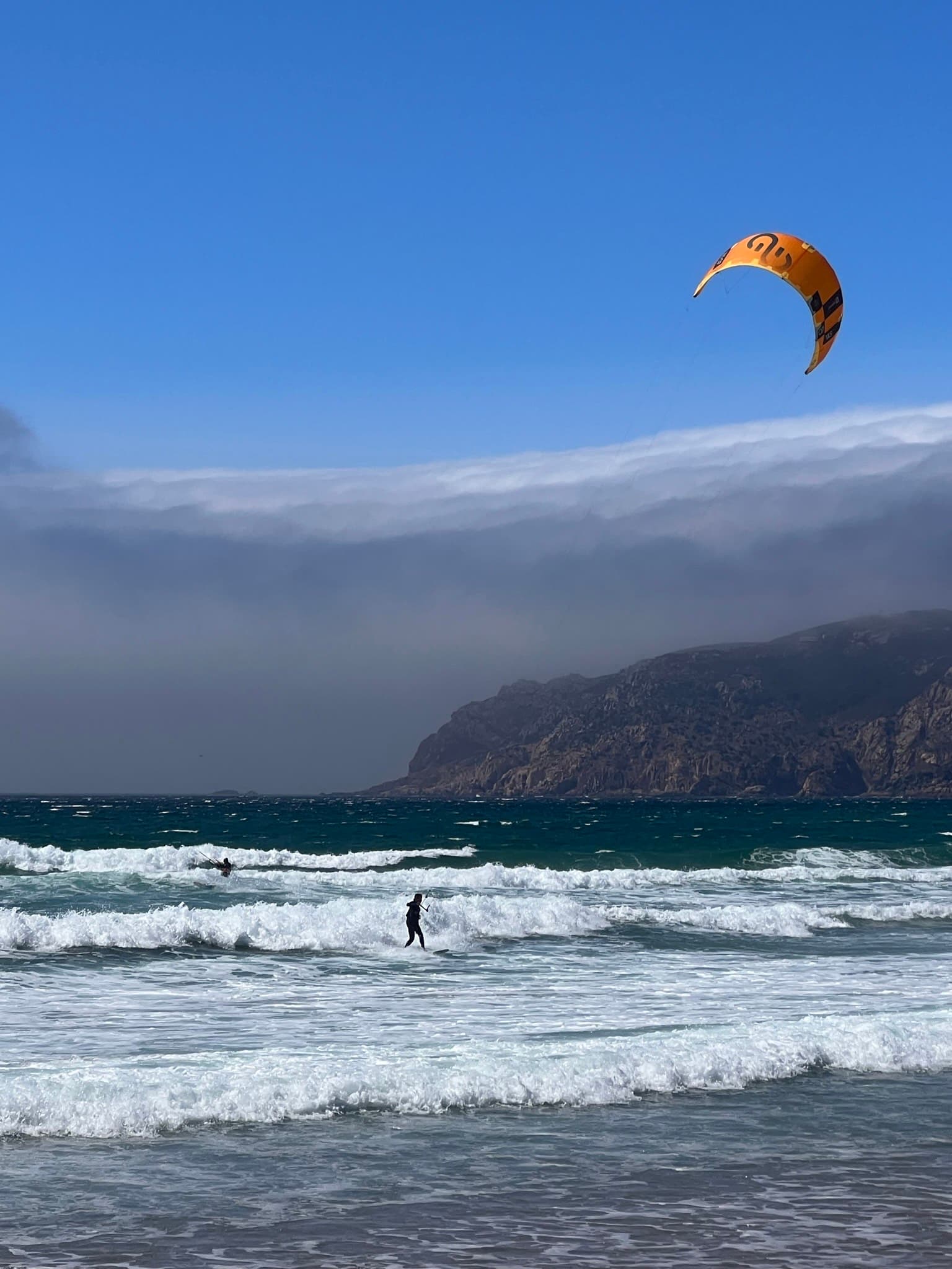 View of a person windsurfing with dramatic cliffs in the distance