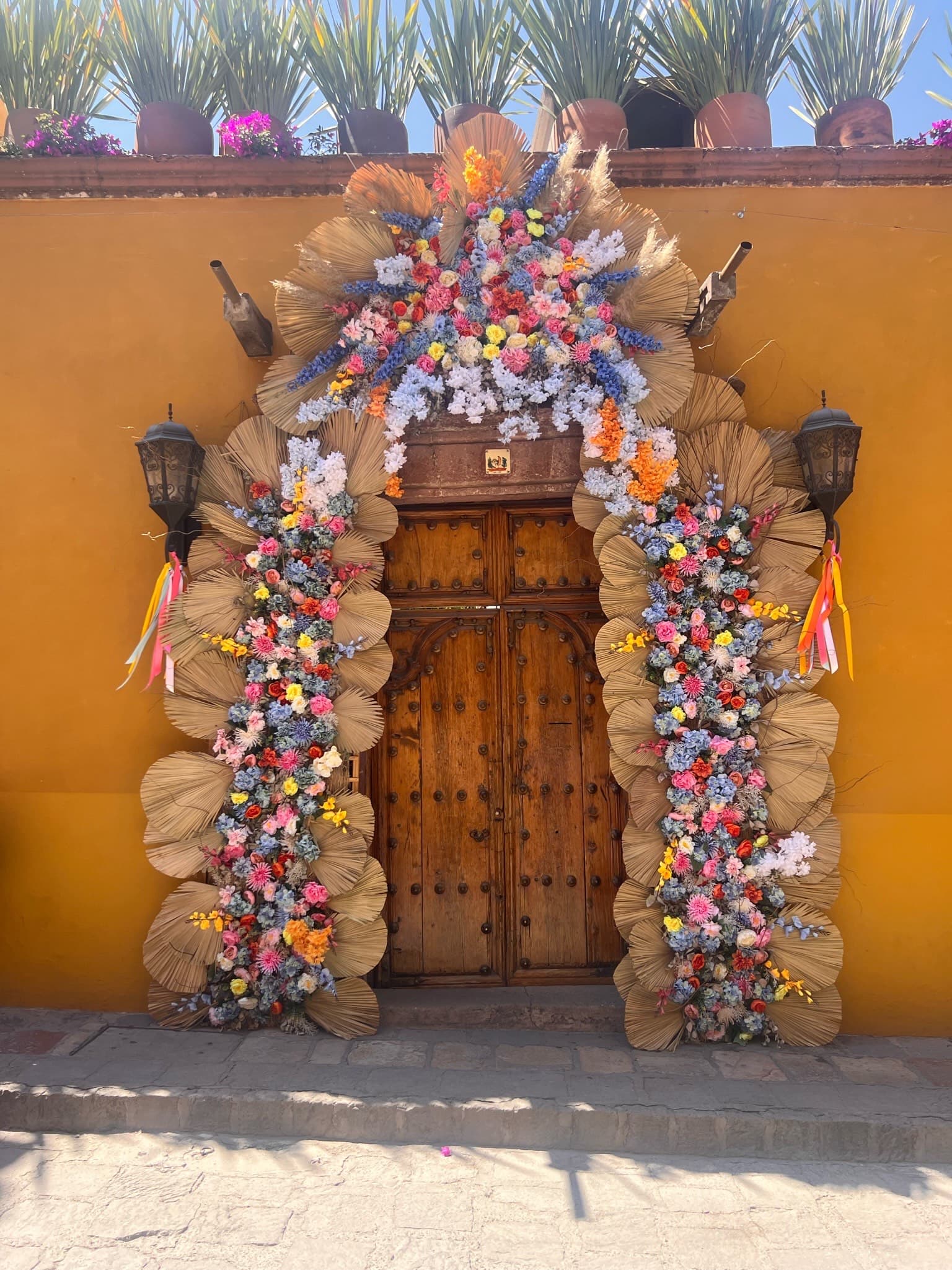 View of a wooden door in a yellow wall decorated with colorful flowers