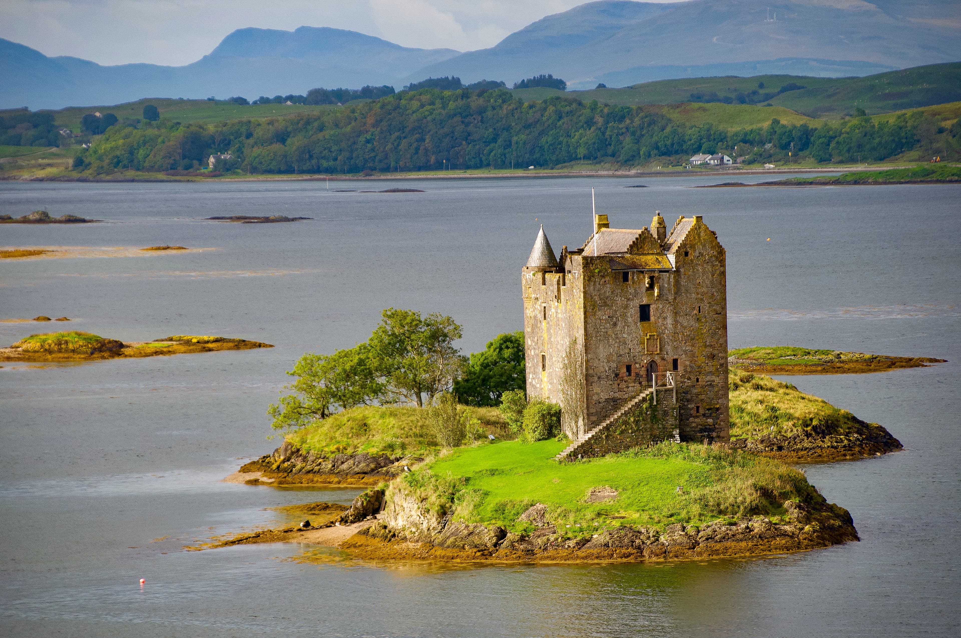 An ancient building sitting on a little island in the ocean.