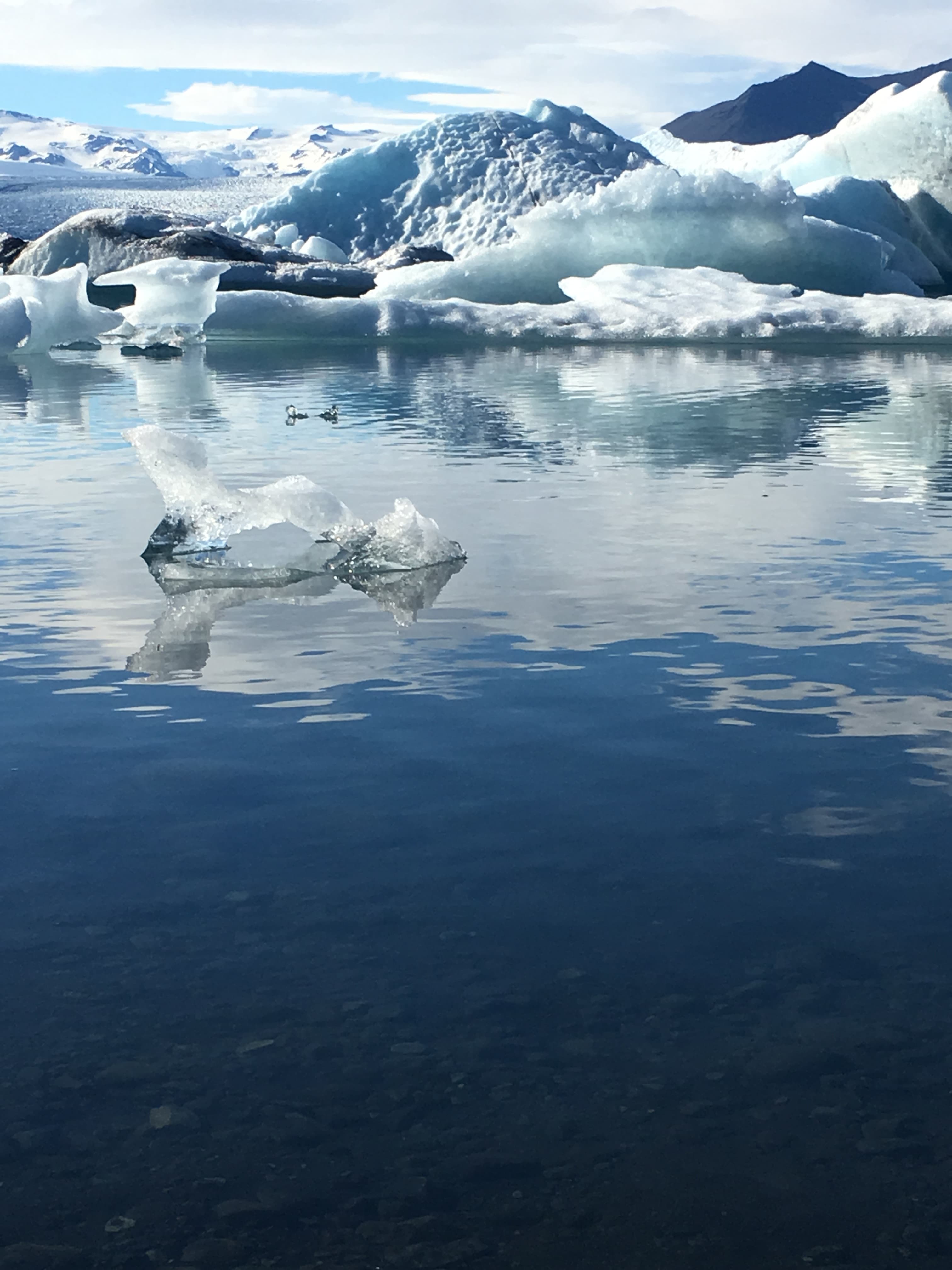 A solitary iceberg drifts in calm waters, with towering mountains rising in the background, creating a stunning natural scene.