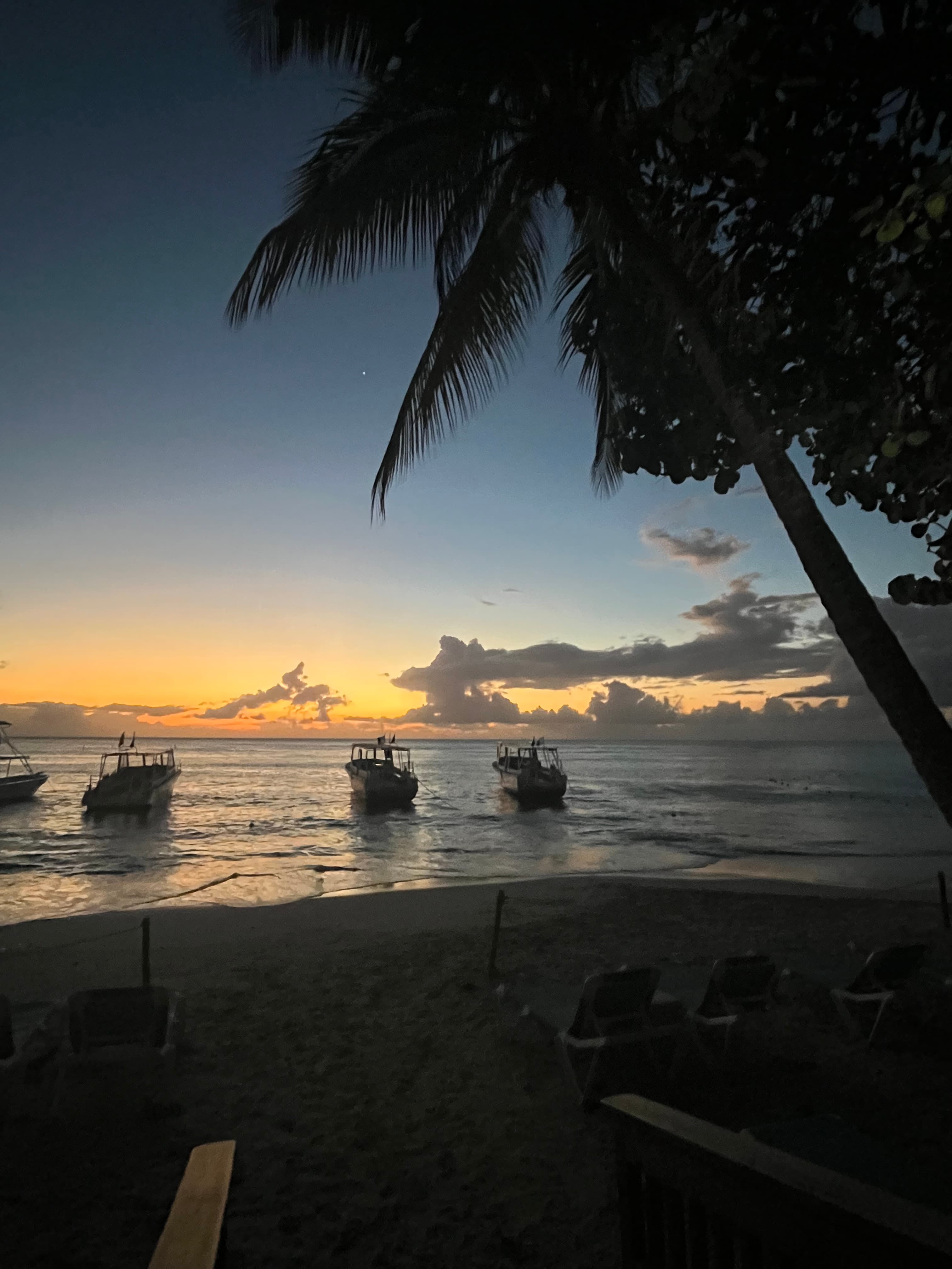 Serene photo of the beach with boats in the water during sunset.