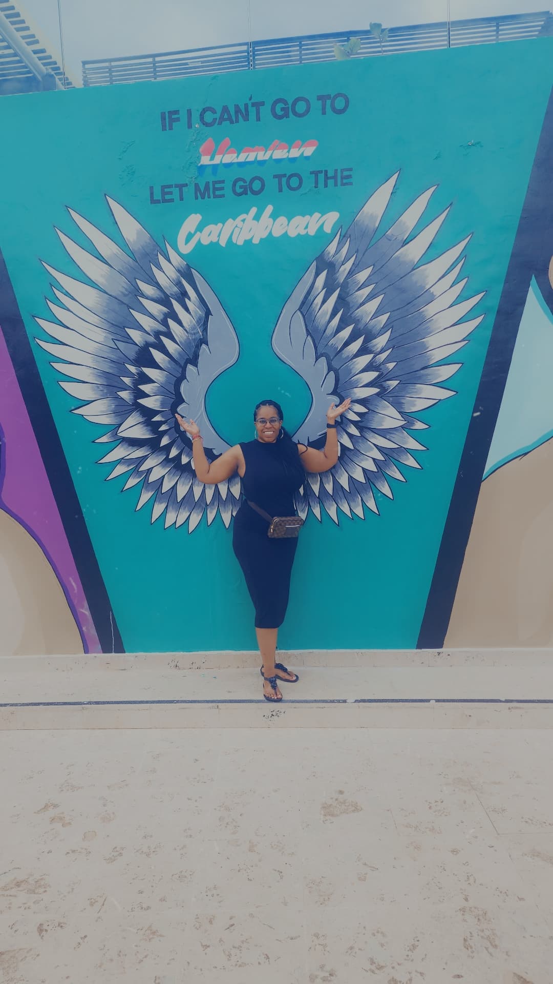 Angel poses in front of a vibrant mural featuring large, colorful wings, creating a striking visual contrast.