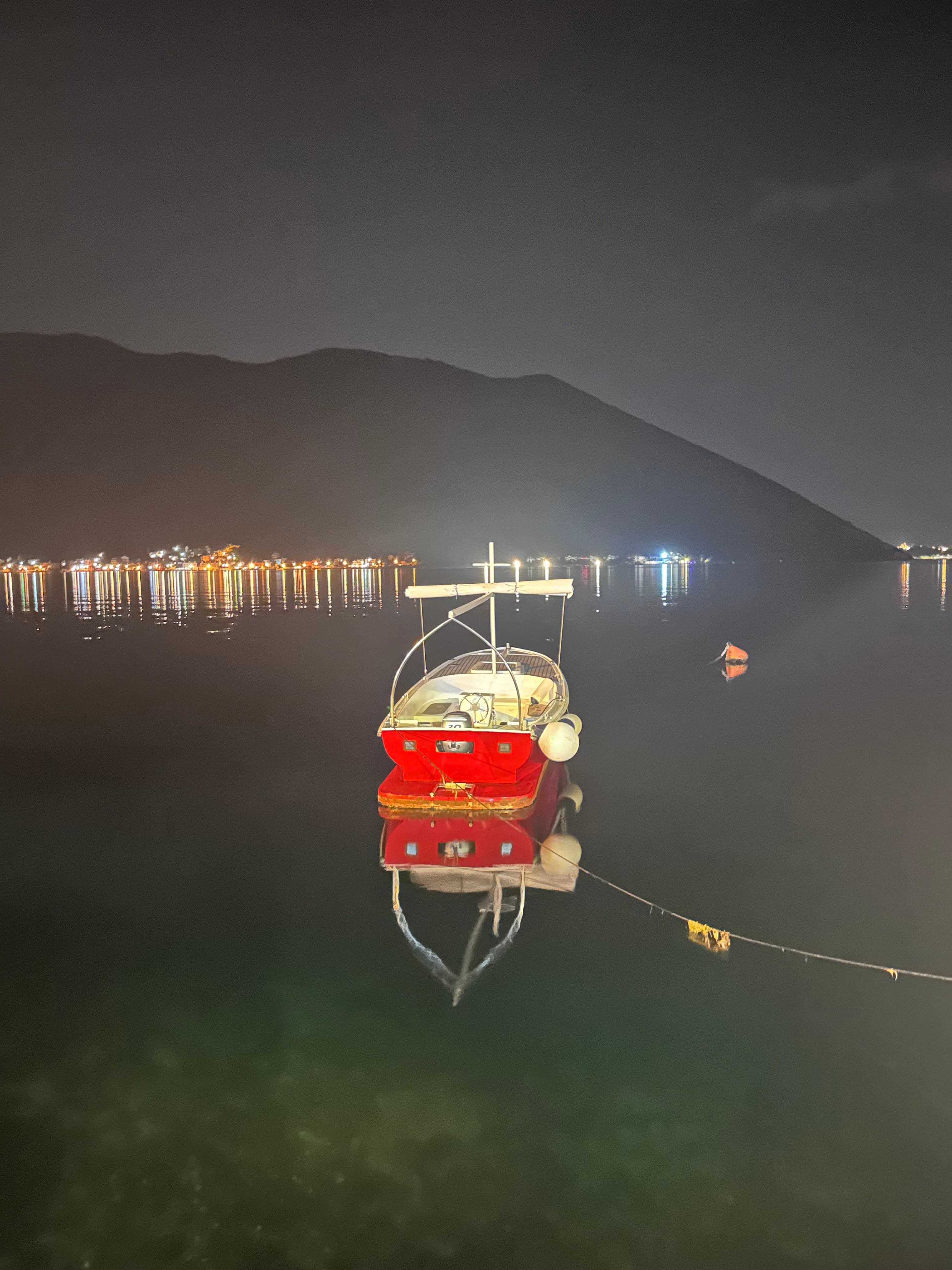 View of a small red boat floating offshore at night