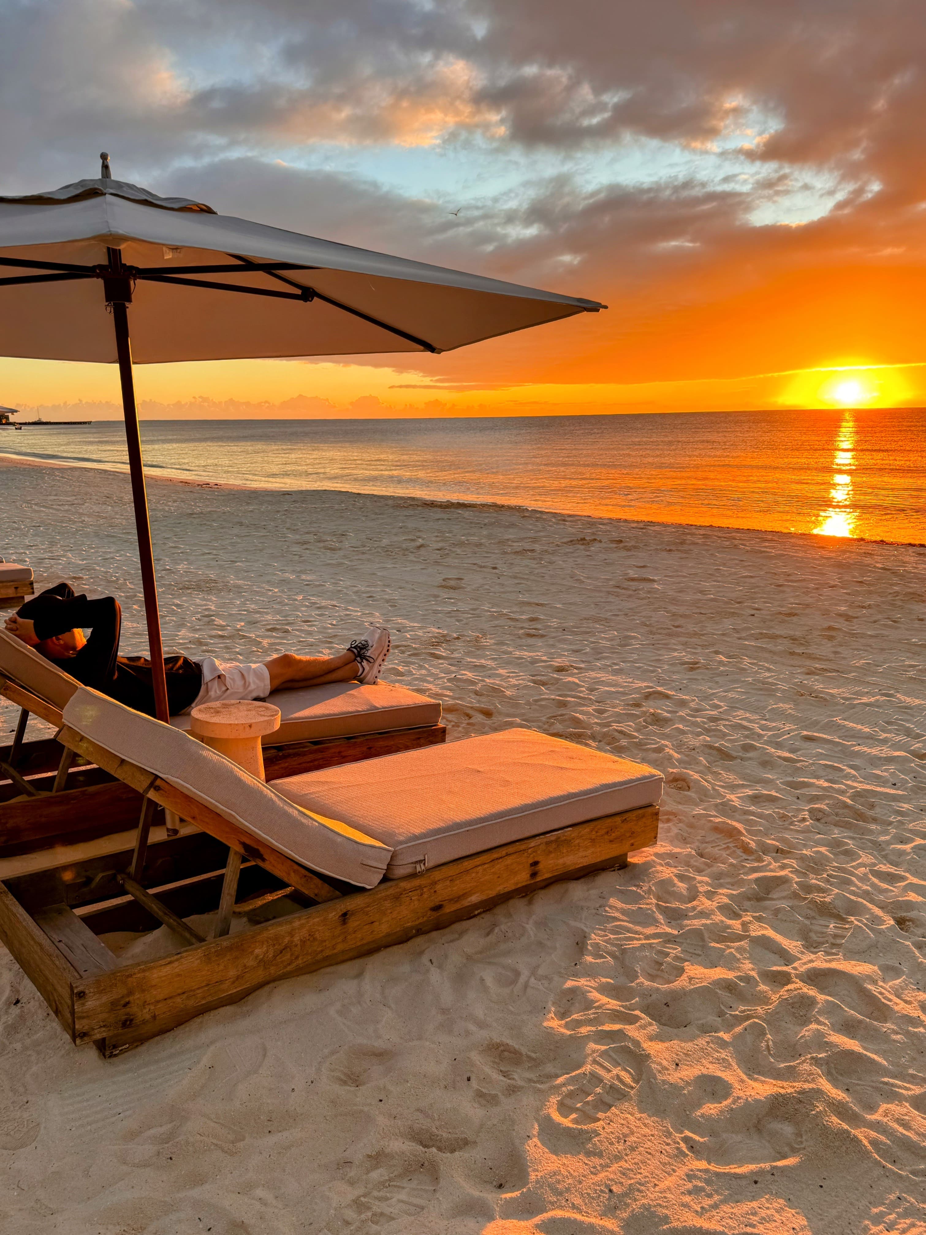 View of padded lounge chairs on the beach at sunset