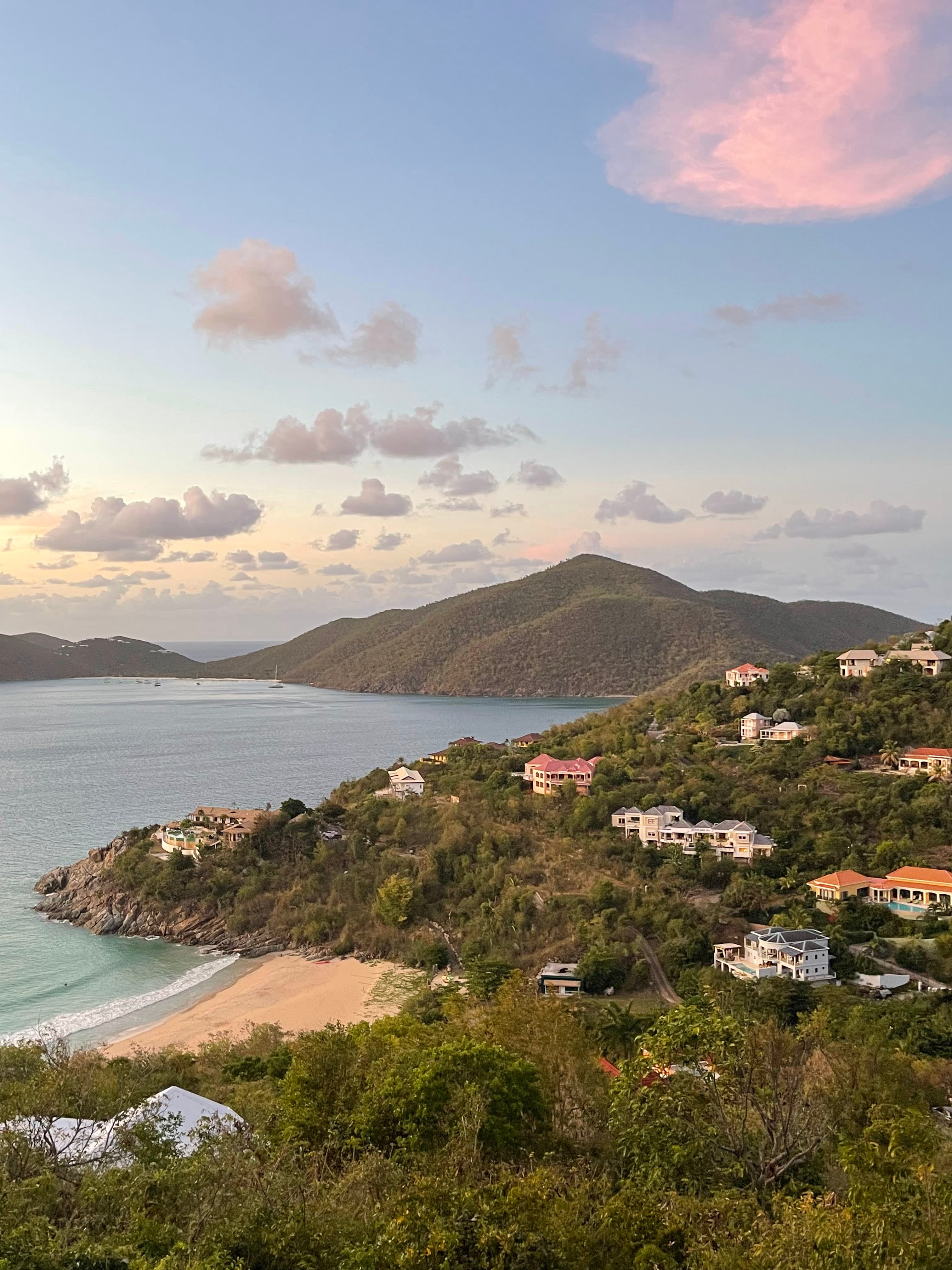 An aerial view of villas tucked into grassy land and island-like terrain against the beach and sea views.