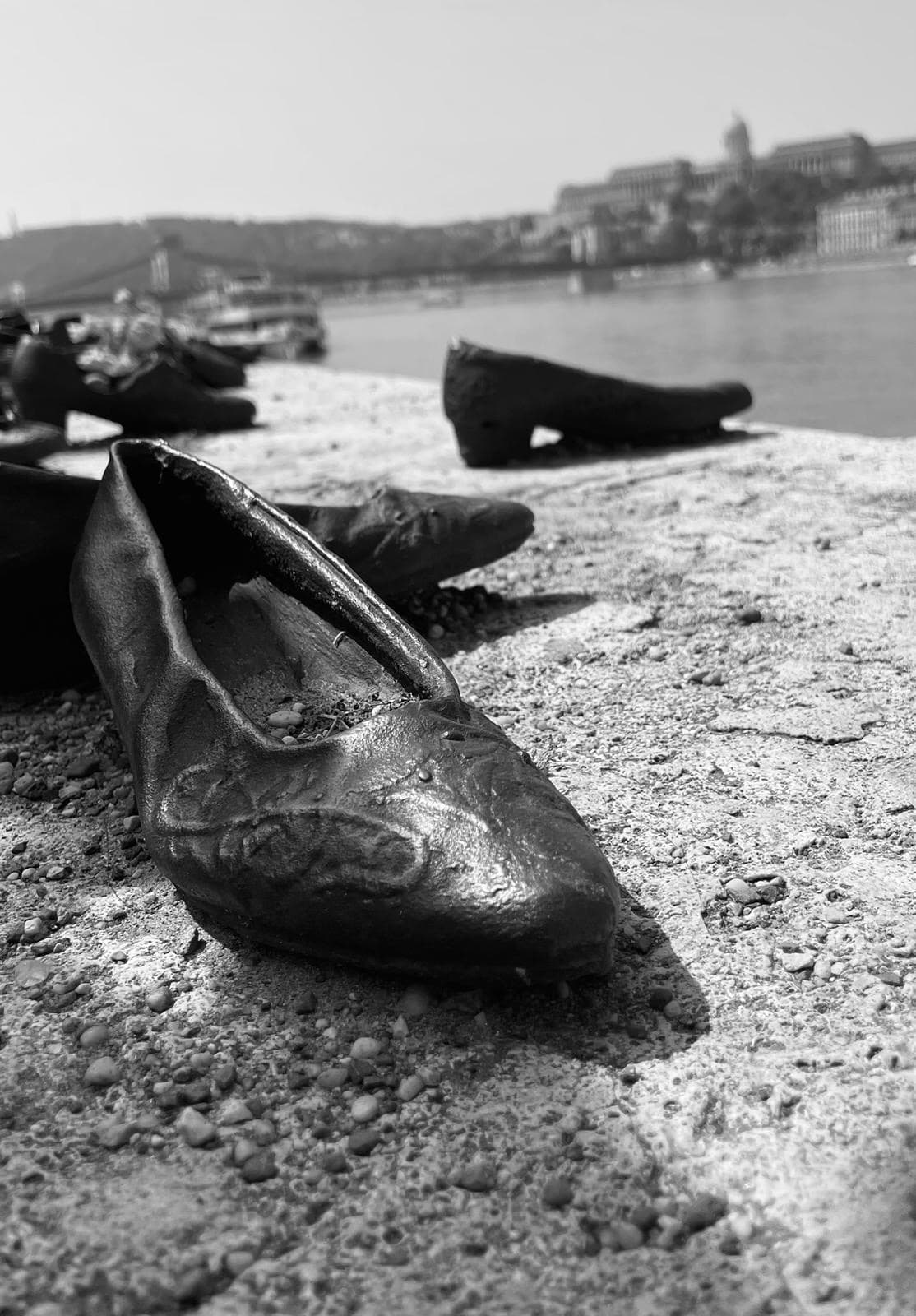 Close up black and white image of a small shoe sculpture alongside a riverbank