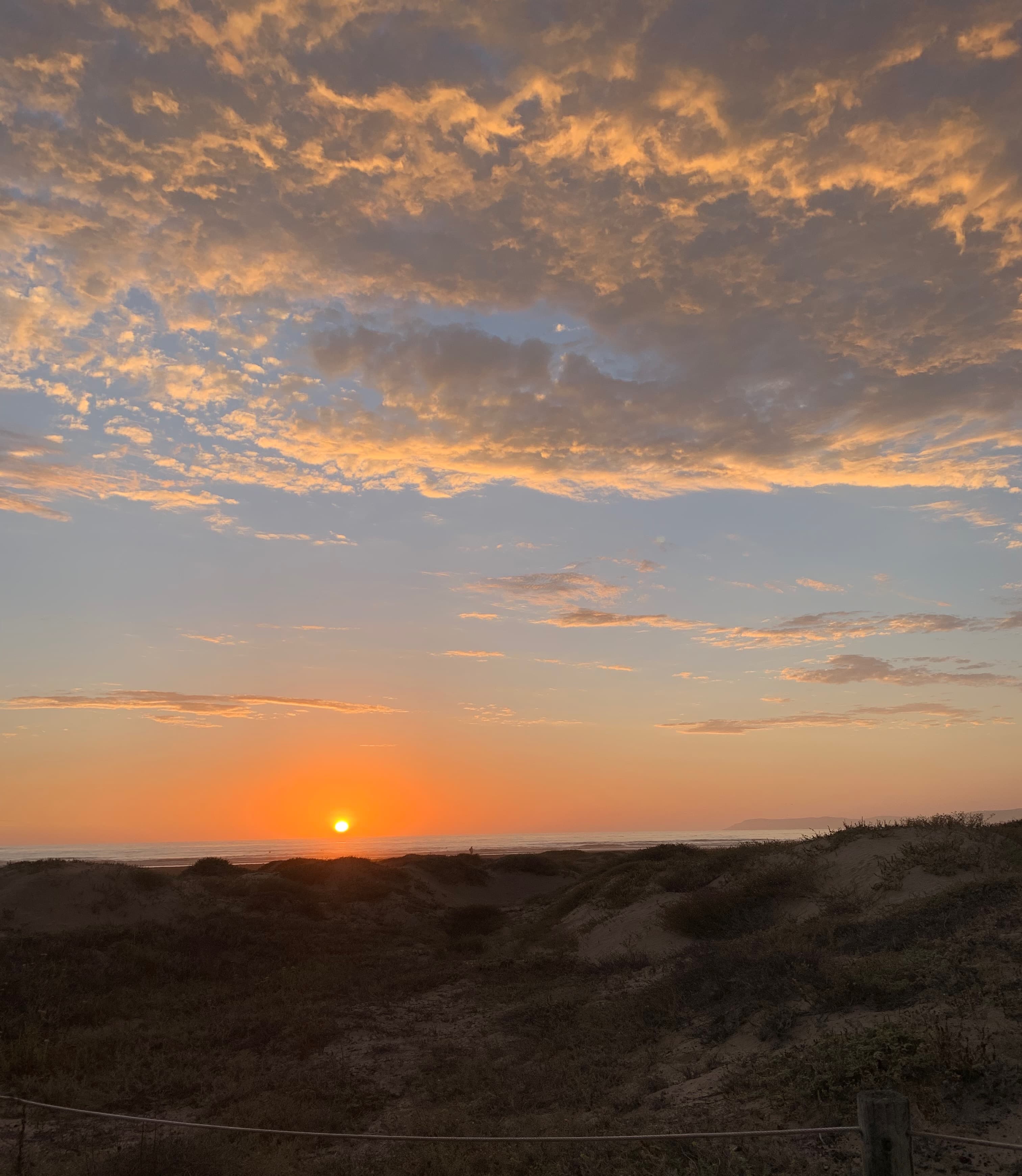 View of a sunset just over the horizon with some clouds above
