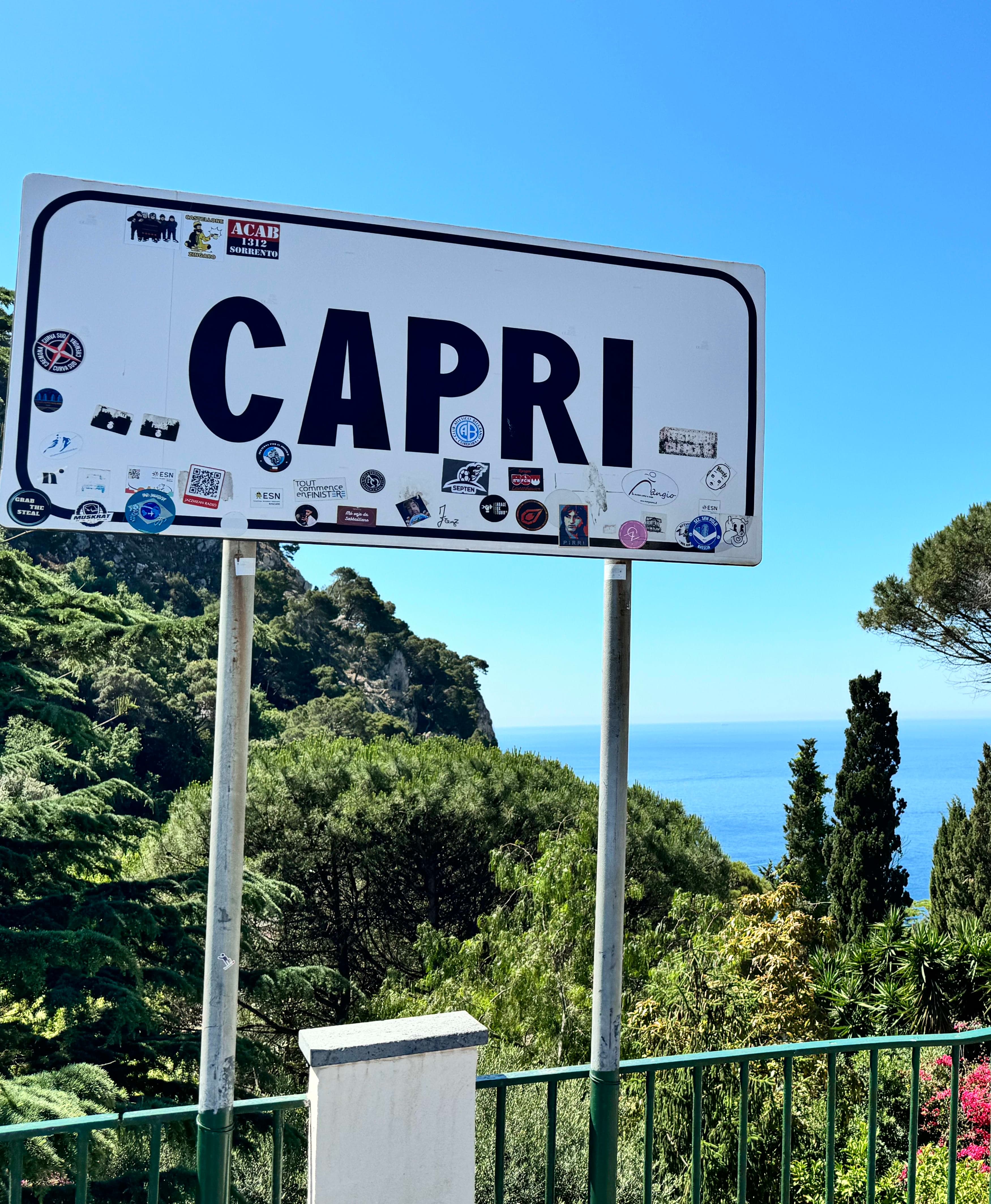 View of a sign for Capri with trees and the ocean visible in the distance on a clear day