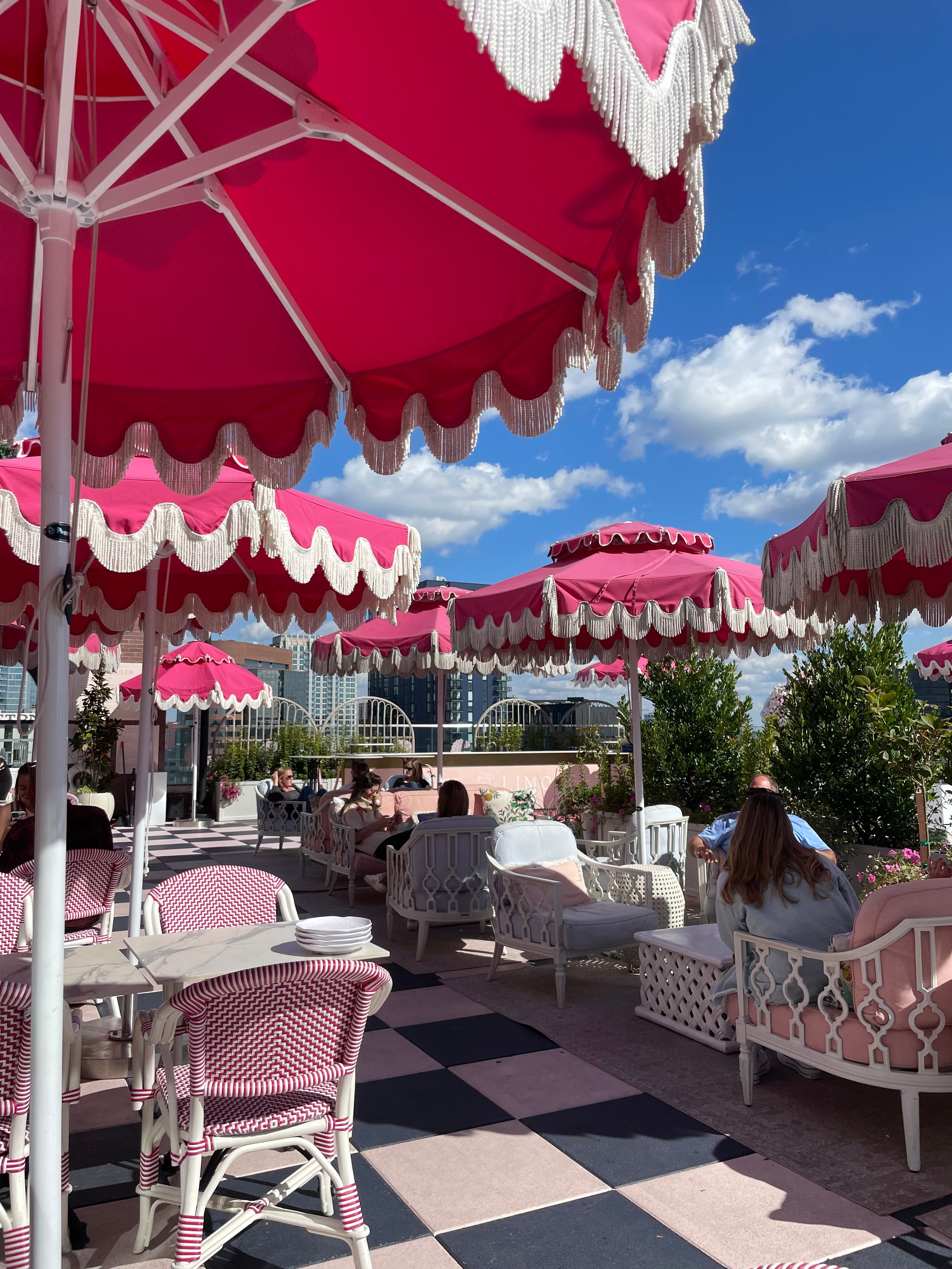A view of an outdoor dining patio with pink and black checkered tile, pink chairs and hot pink umbrellas during the day.