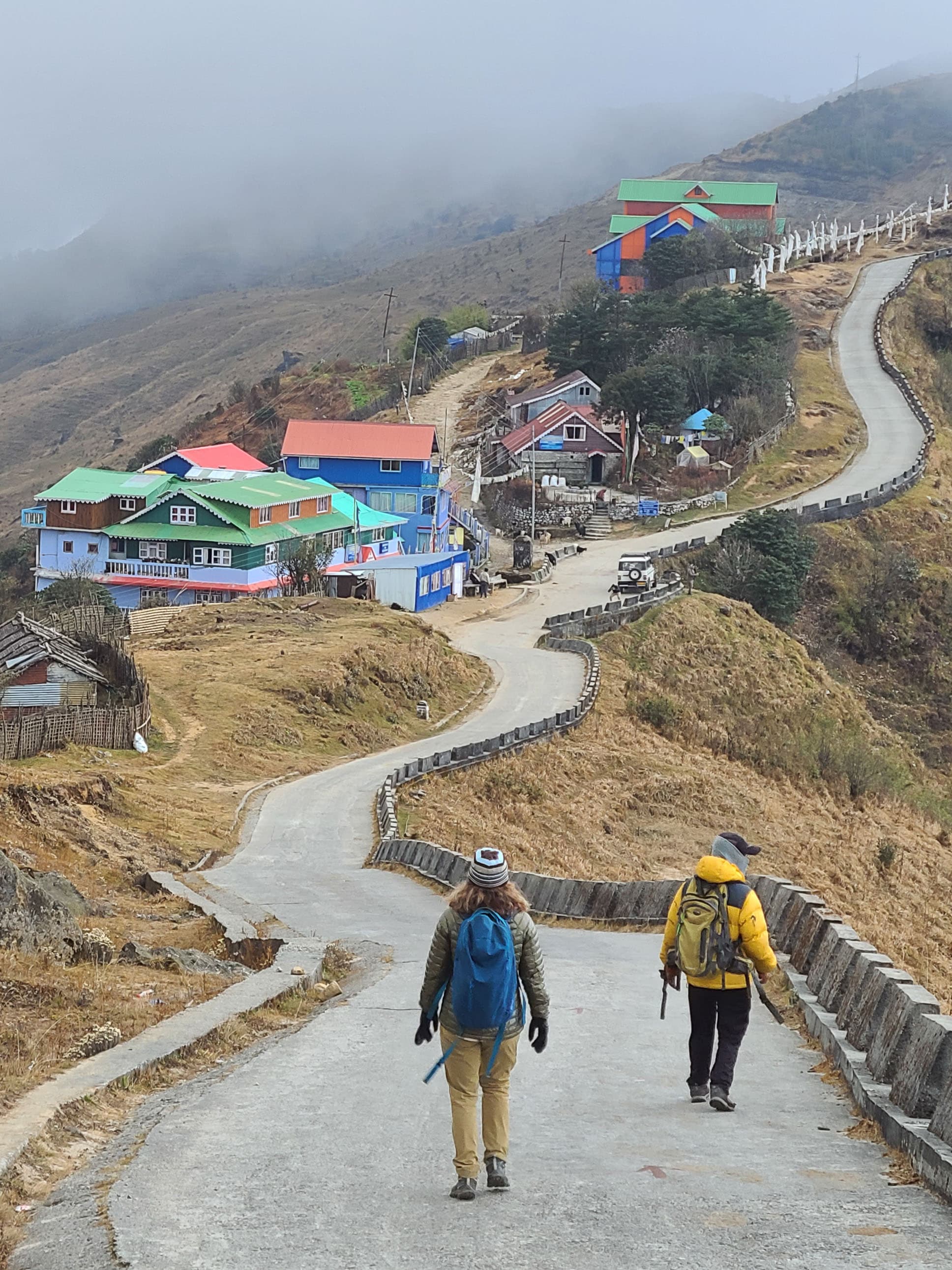 Two backpackers traverse a hilltop town on a misty day.