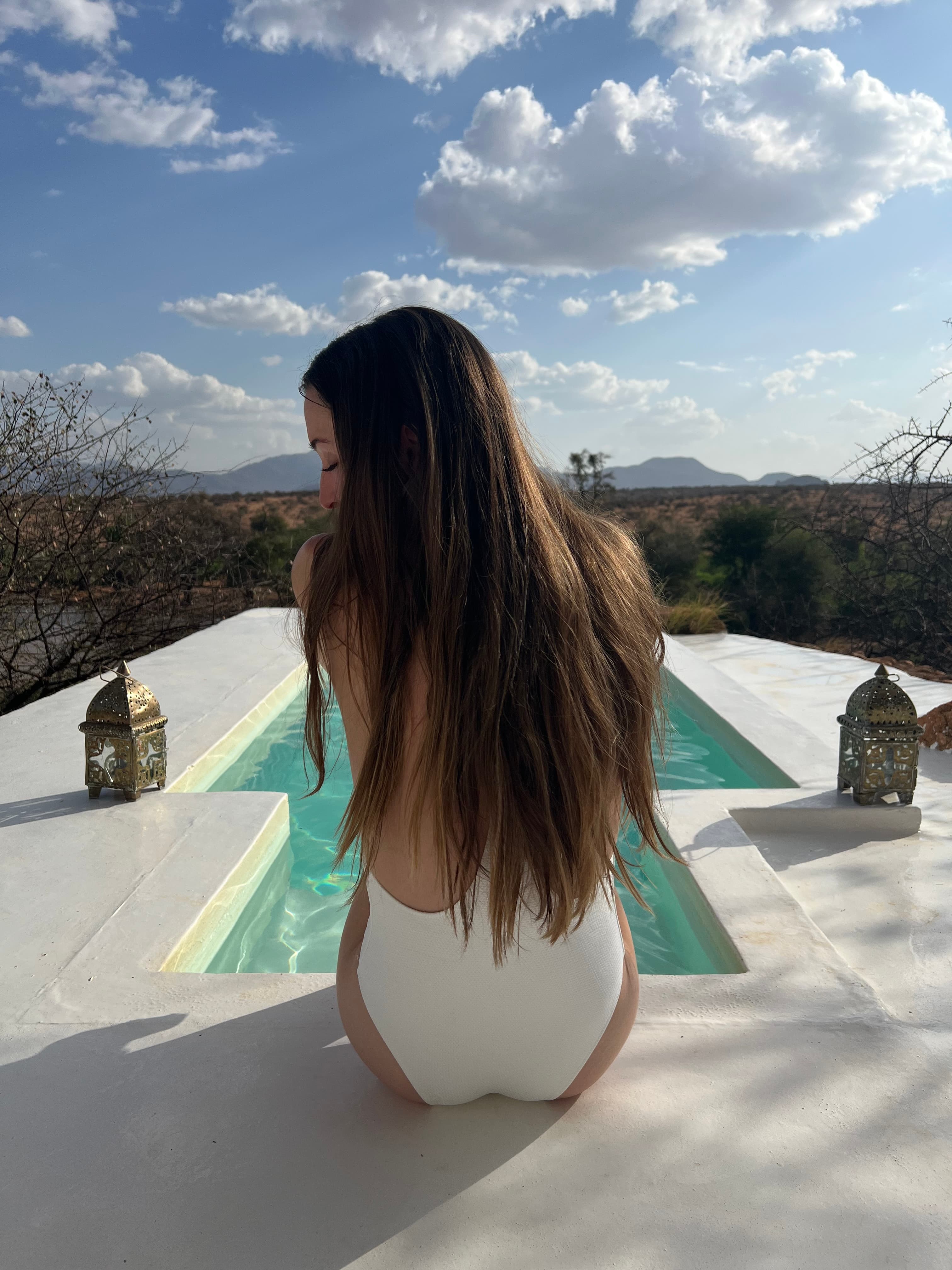 Advisor sitting beside a modern pool in a white one-piece bathing suit