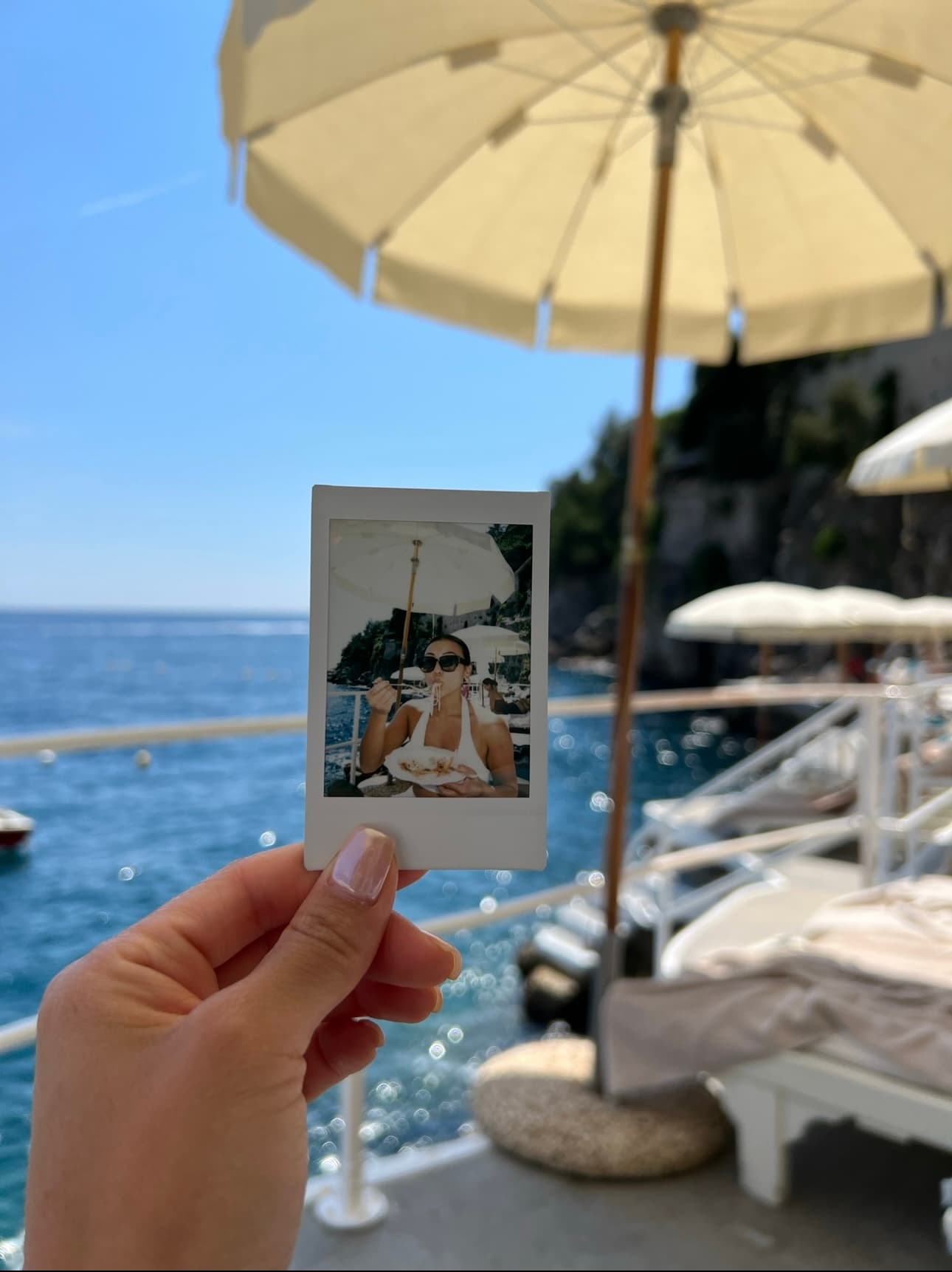 View of a hand holding up a Polaroid of advisor with the sea in the background