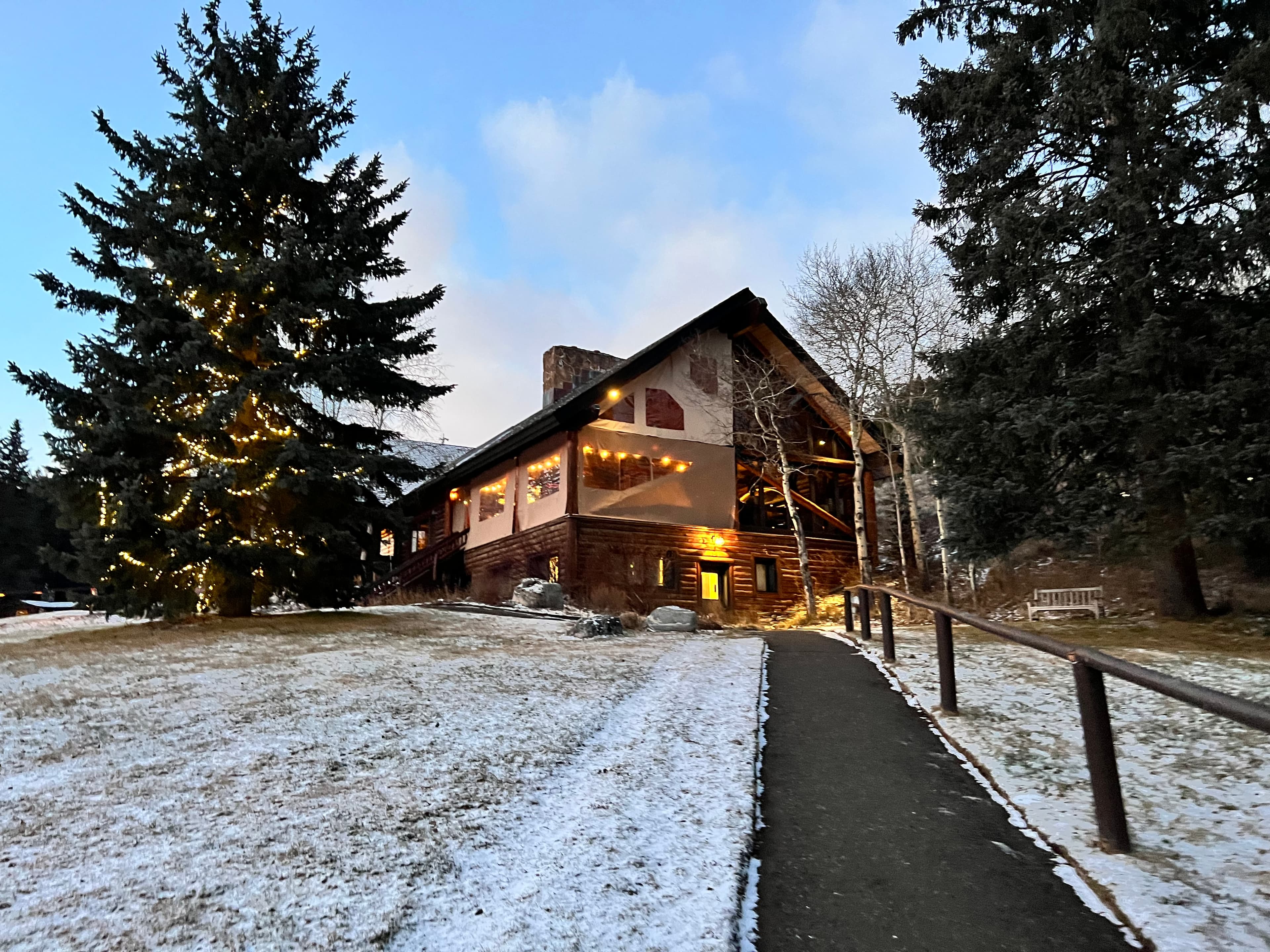 A narrow road leading uphill towards a welcoming lodge with snow on the ground around it