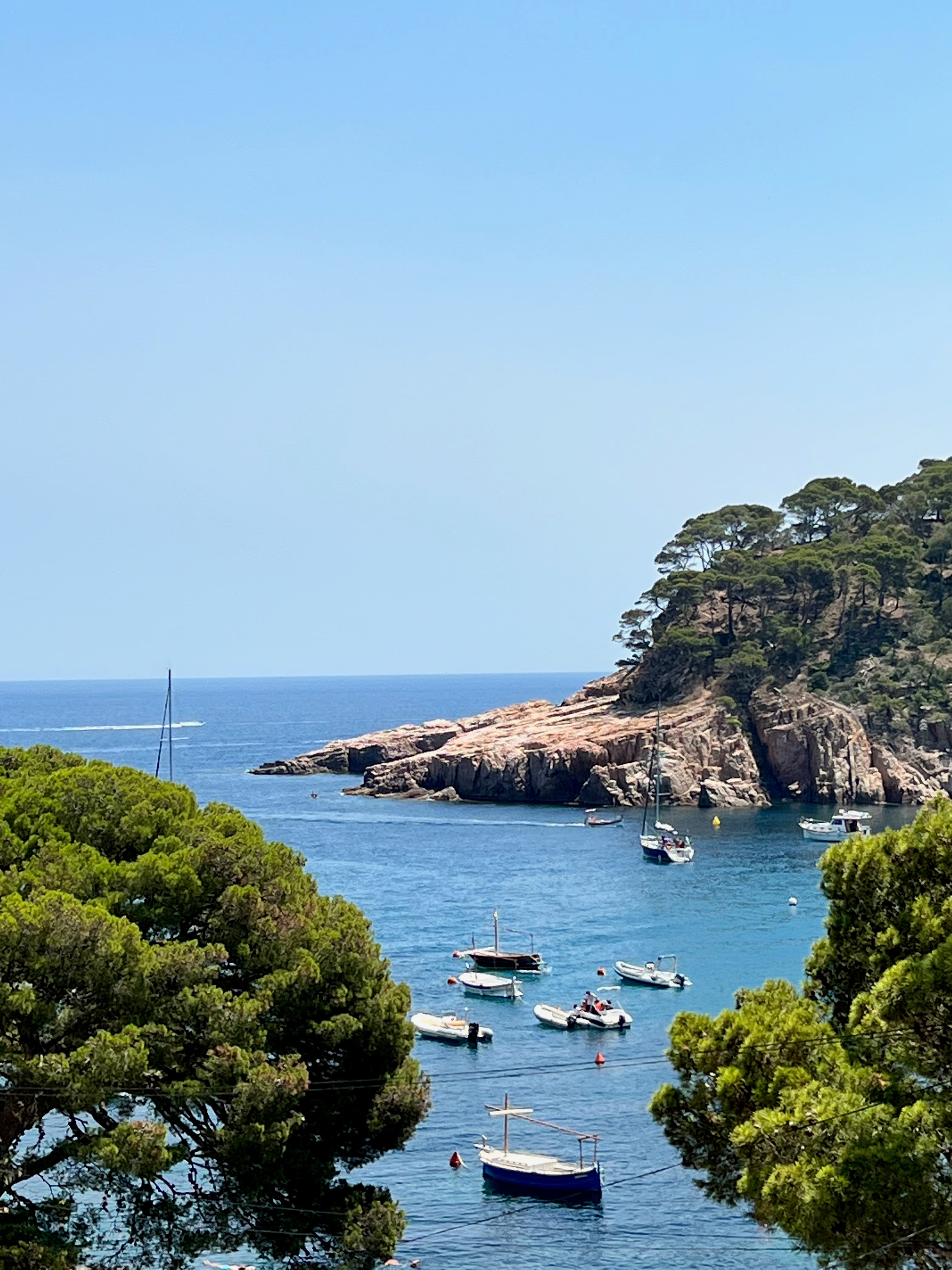 View of a bay lined with rocky cliffs and small boats floating offshore under clear skies