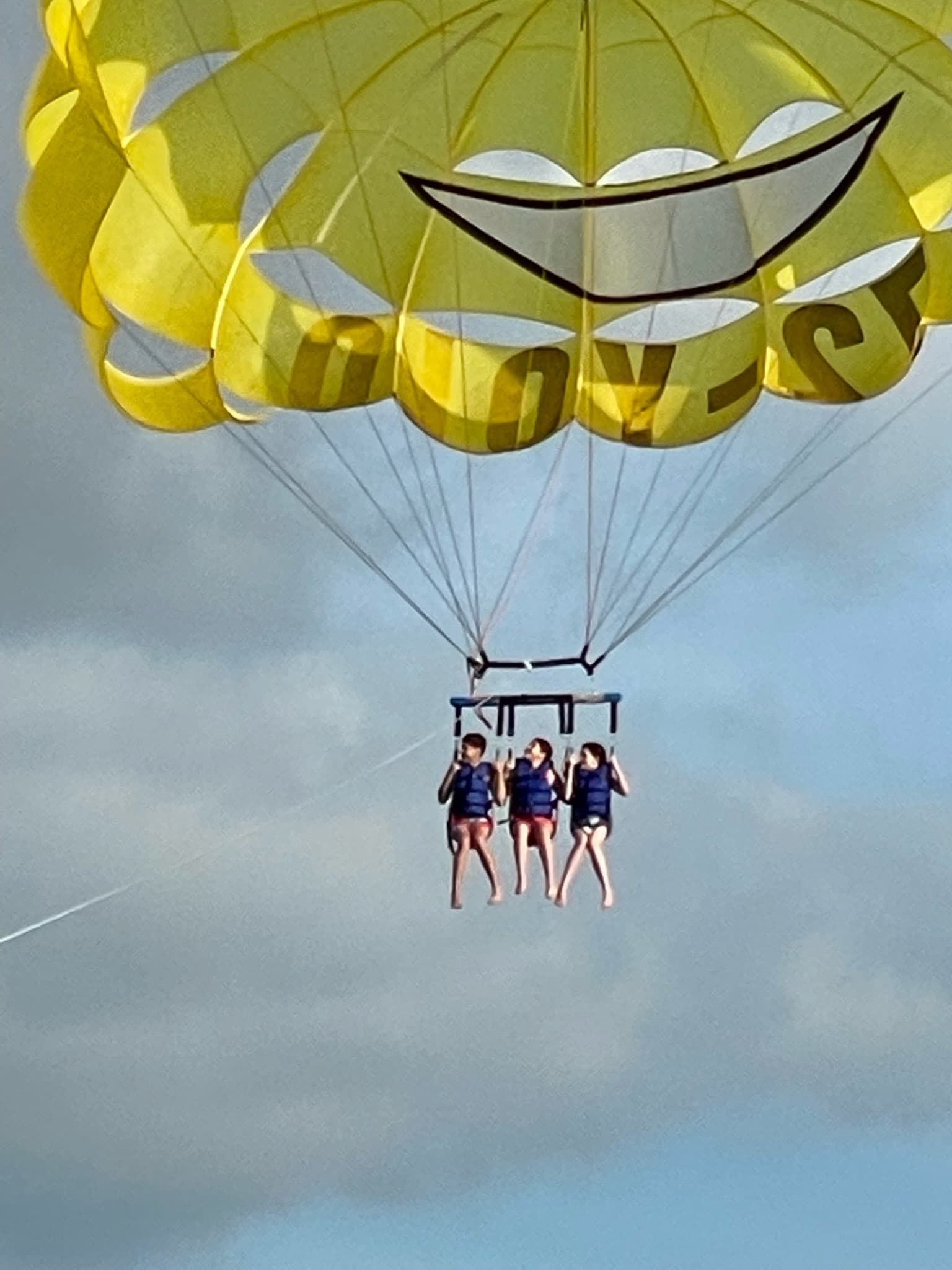 Three people seen mid-air paragliding on a cloudy day