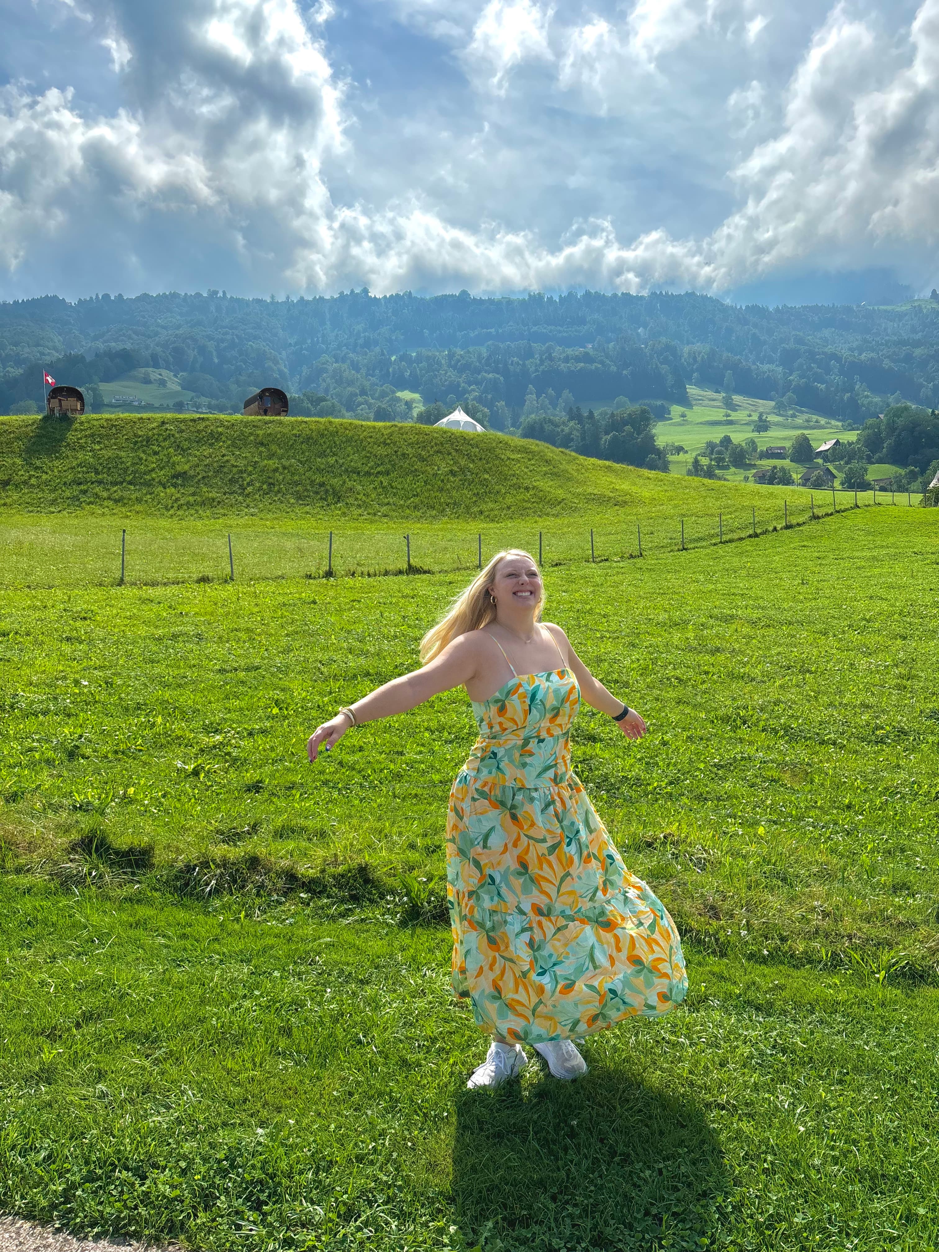 Advisor wearing a long floral print dress and twirling around in a green field