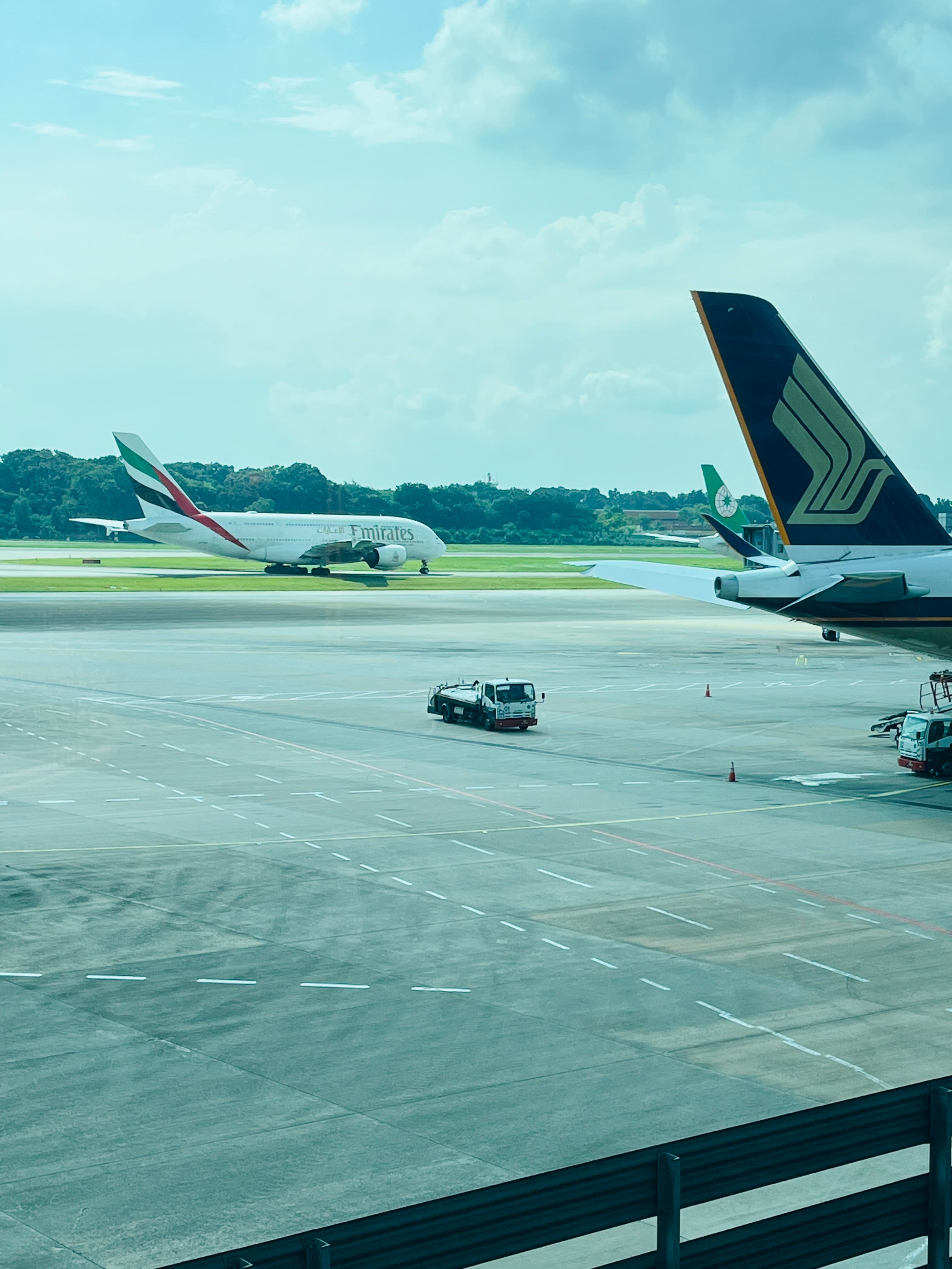 View of an airport tarmac and wing of a plane seen from a window during the day