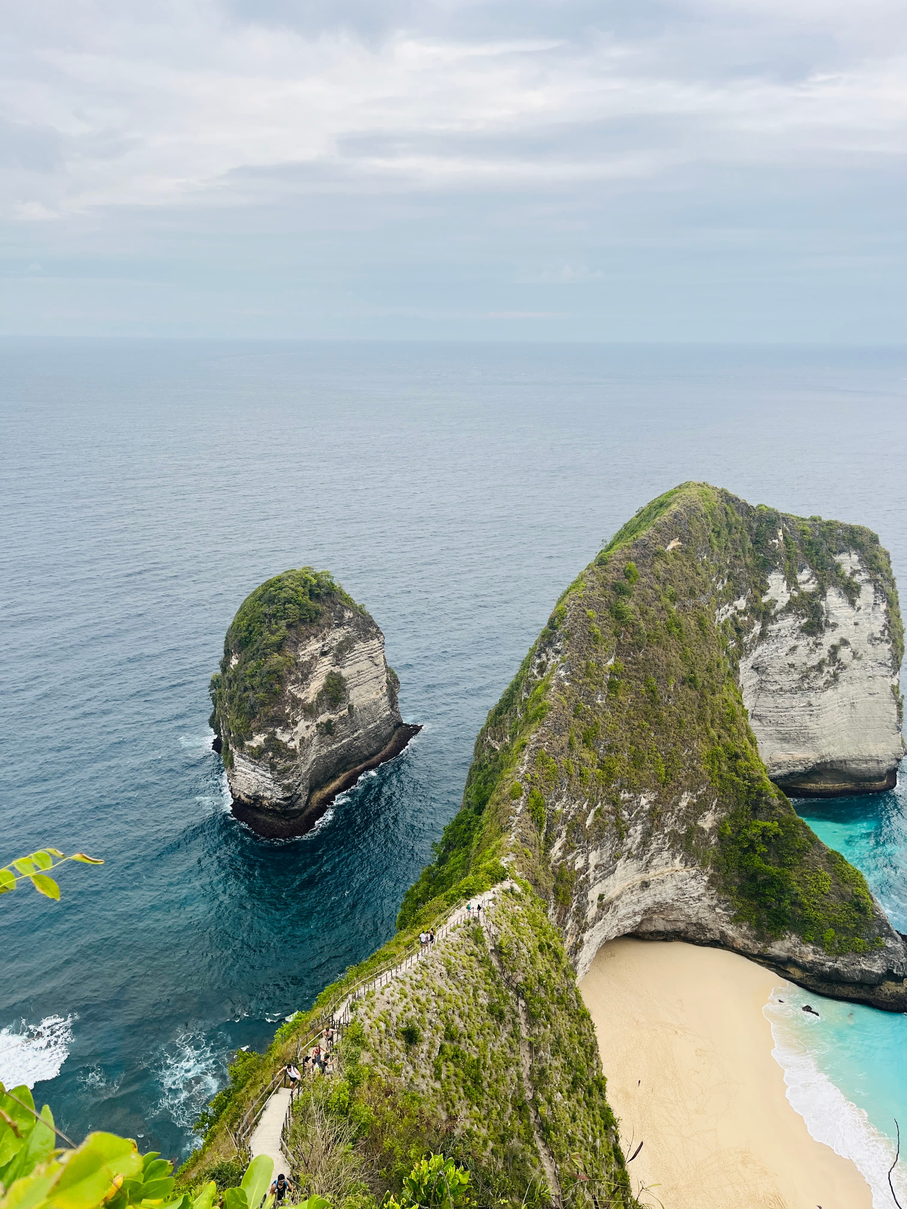 Aerial view of rocky cliffs and a pristine white sand beach in a cove on a cloudy day