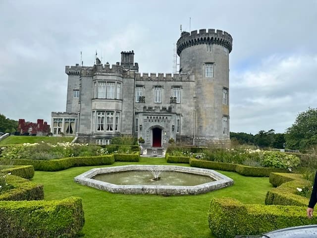 View of a grey castle with green manicured lawns in front on a cloudy day
