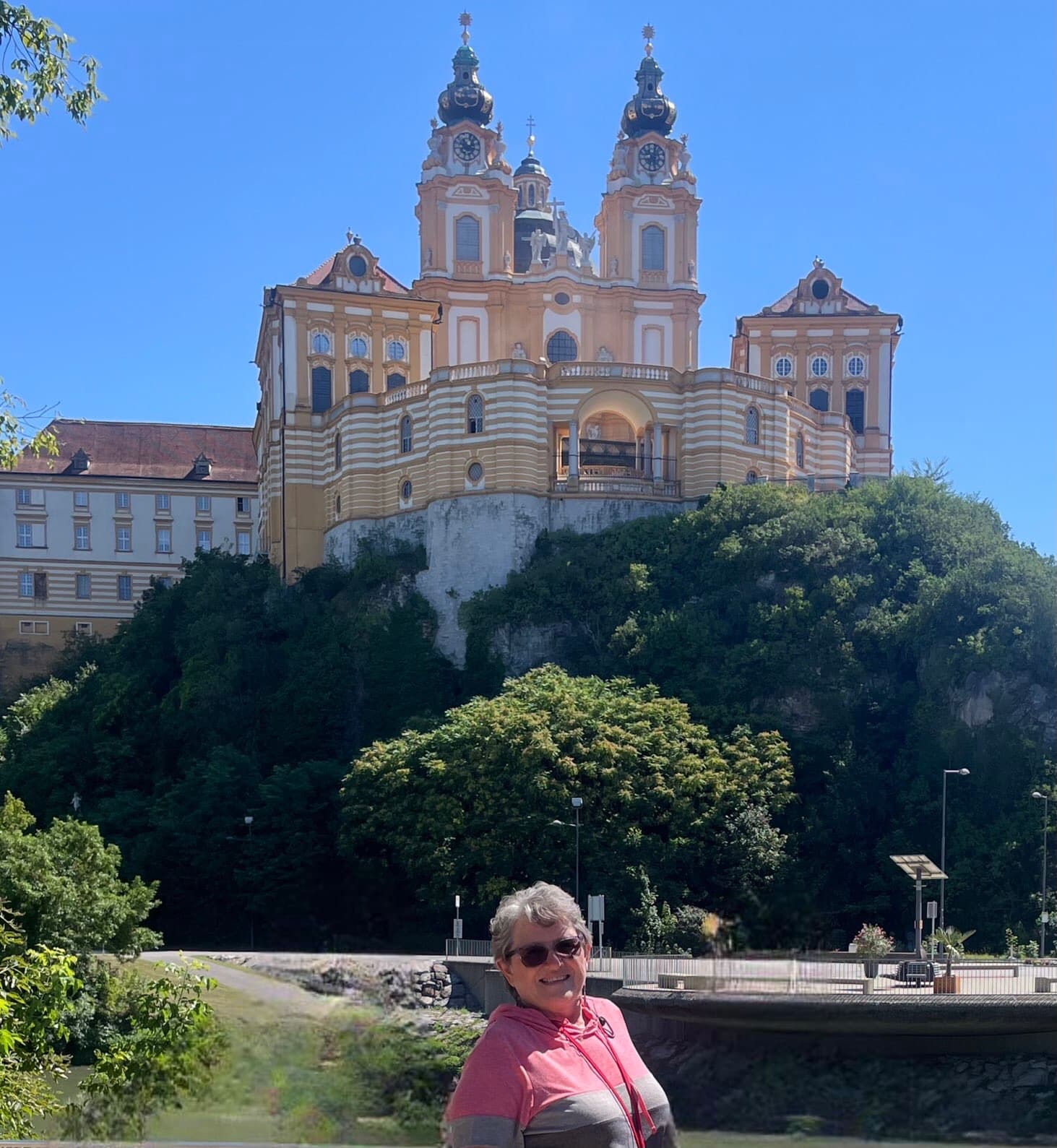 Advisor smiling for a photo outdoors in a park with a beautiful yellow and white building visible behind her on a clear day