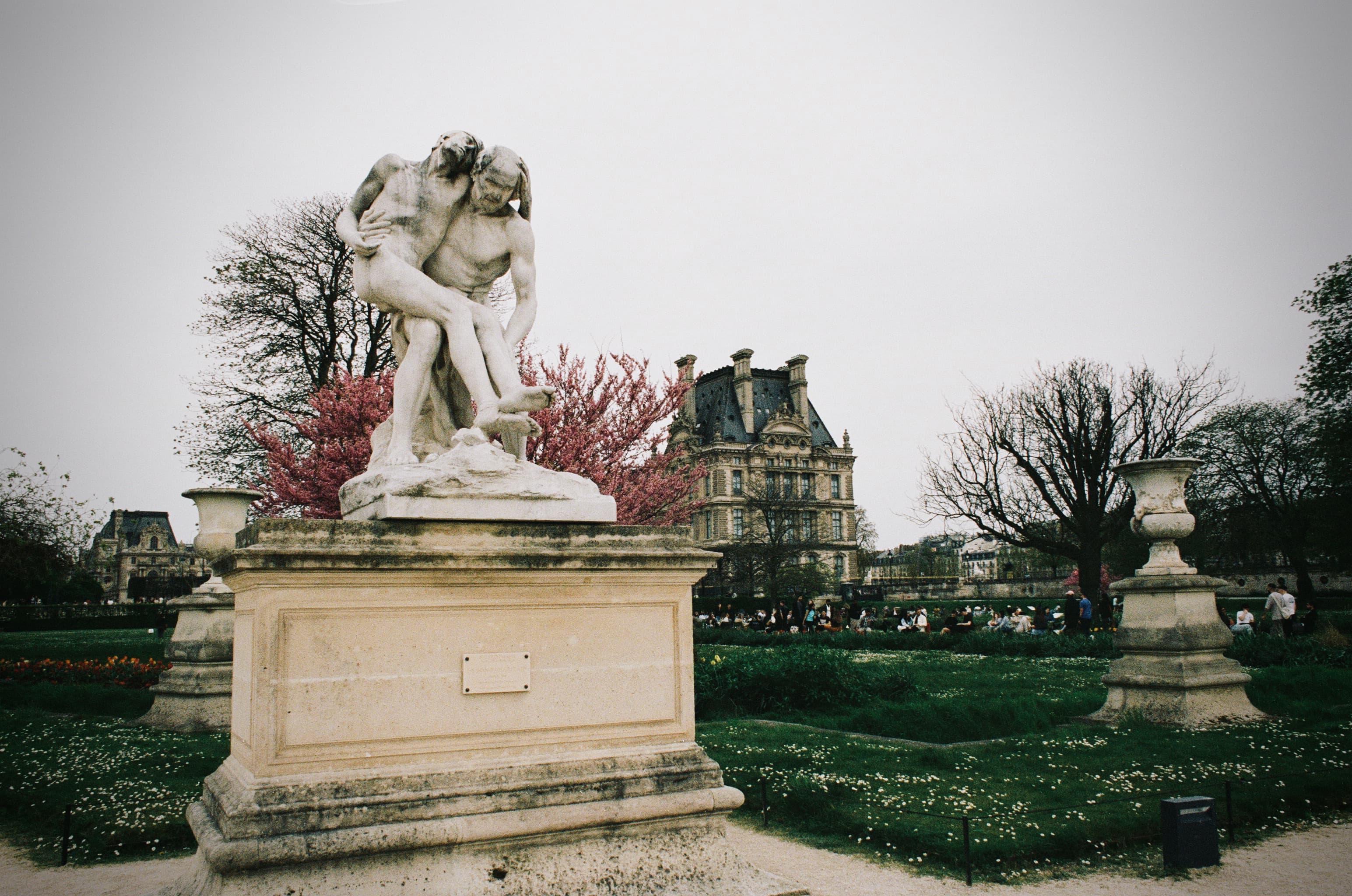 A large white statue of two people holding one another in a city park on a cloudy day