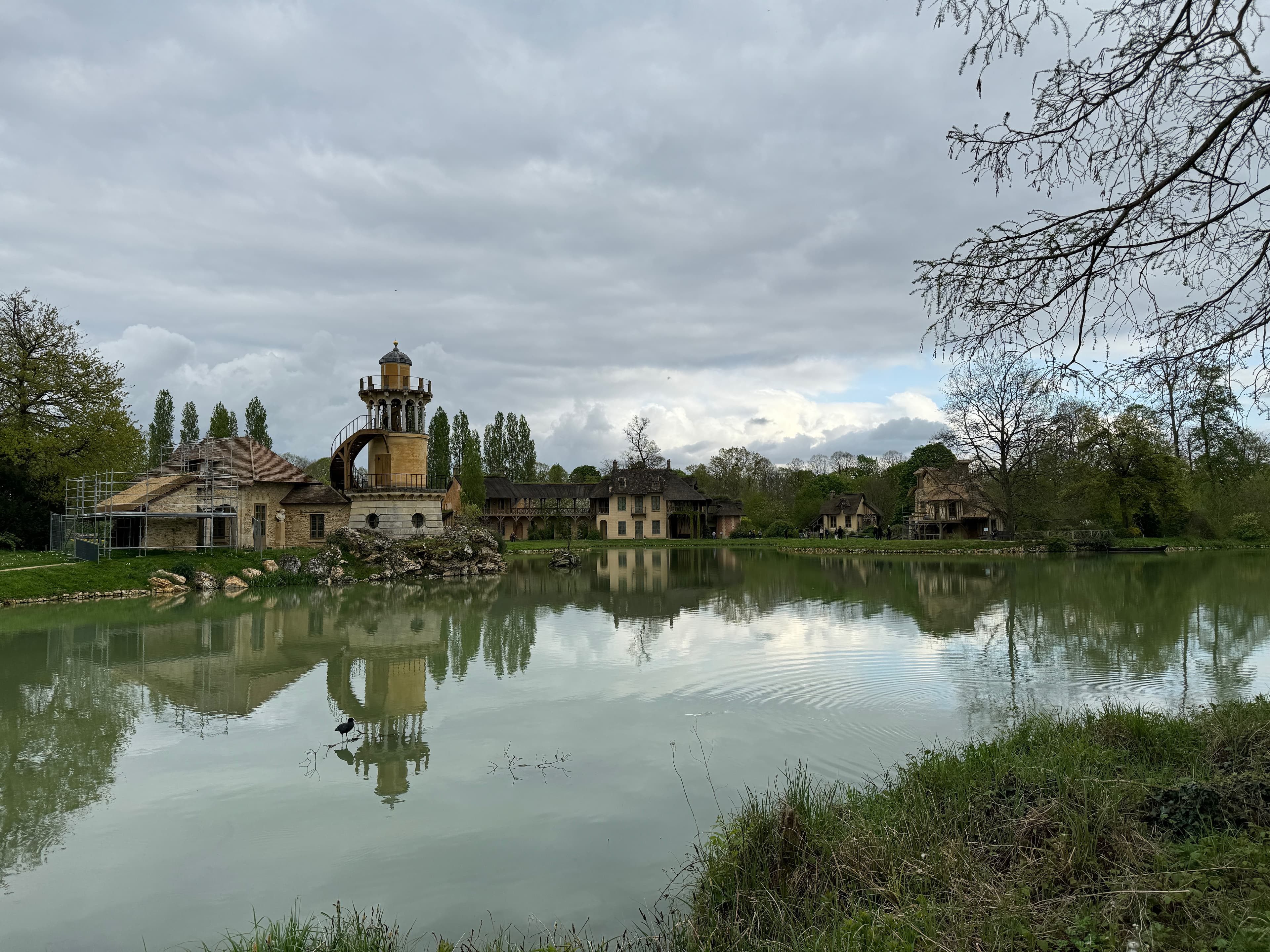 View of a glassy pond with a pretty old building on the far side under cloudy skies