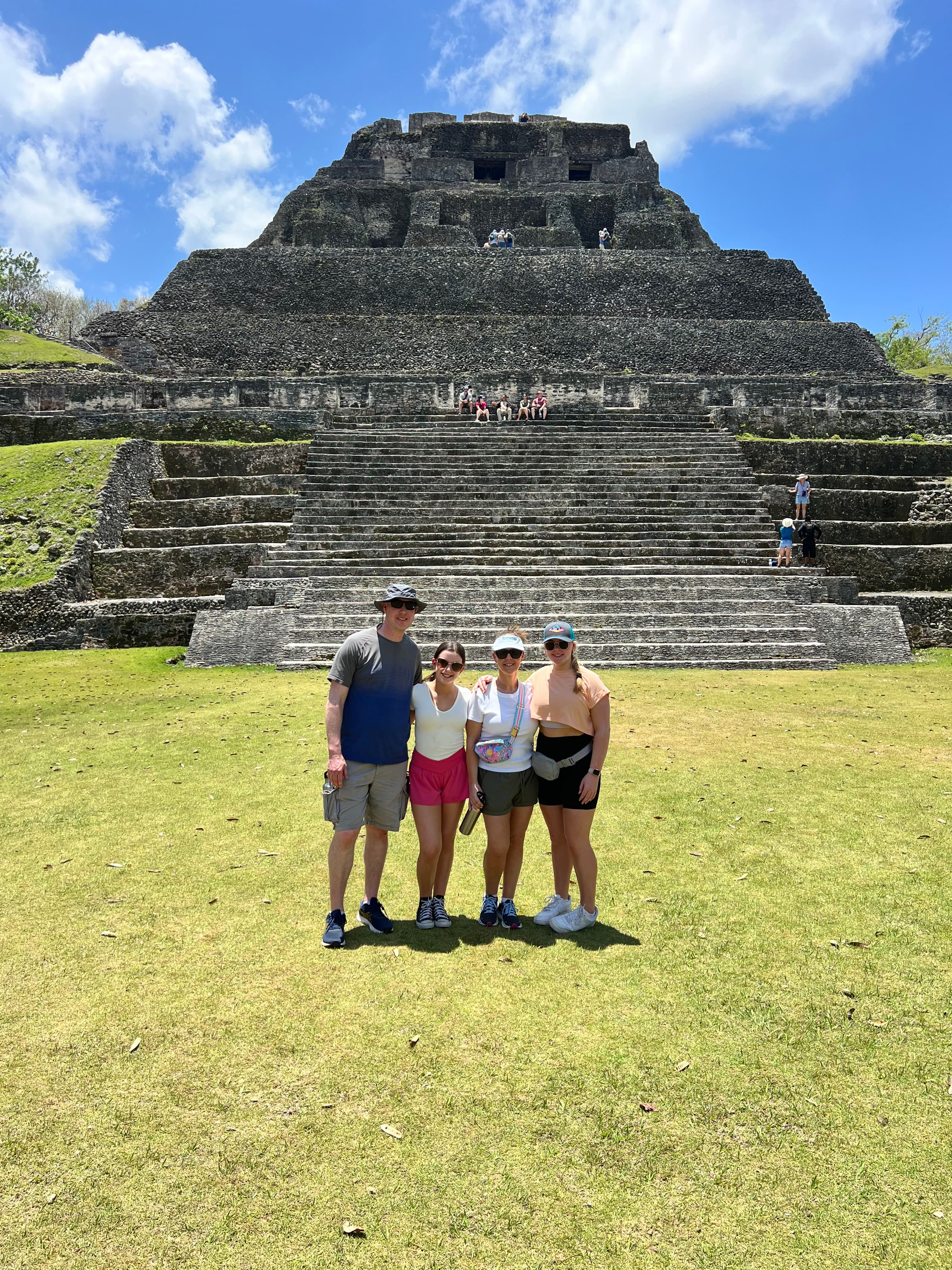 Advisor and family posing side by side on a grassy lawn in front of an ancient stone pyramid on a sunny day