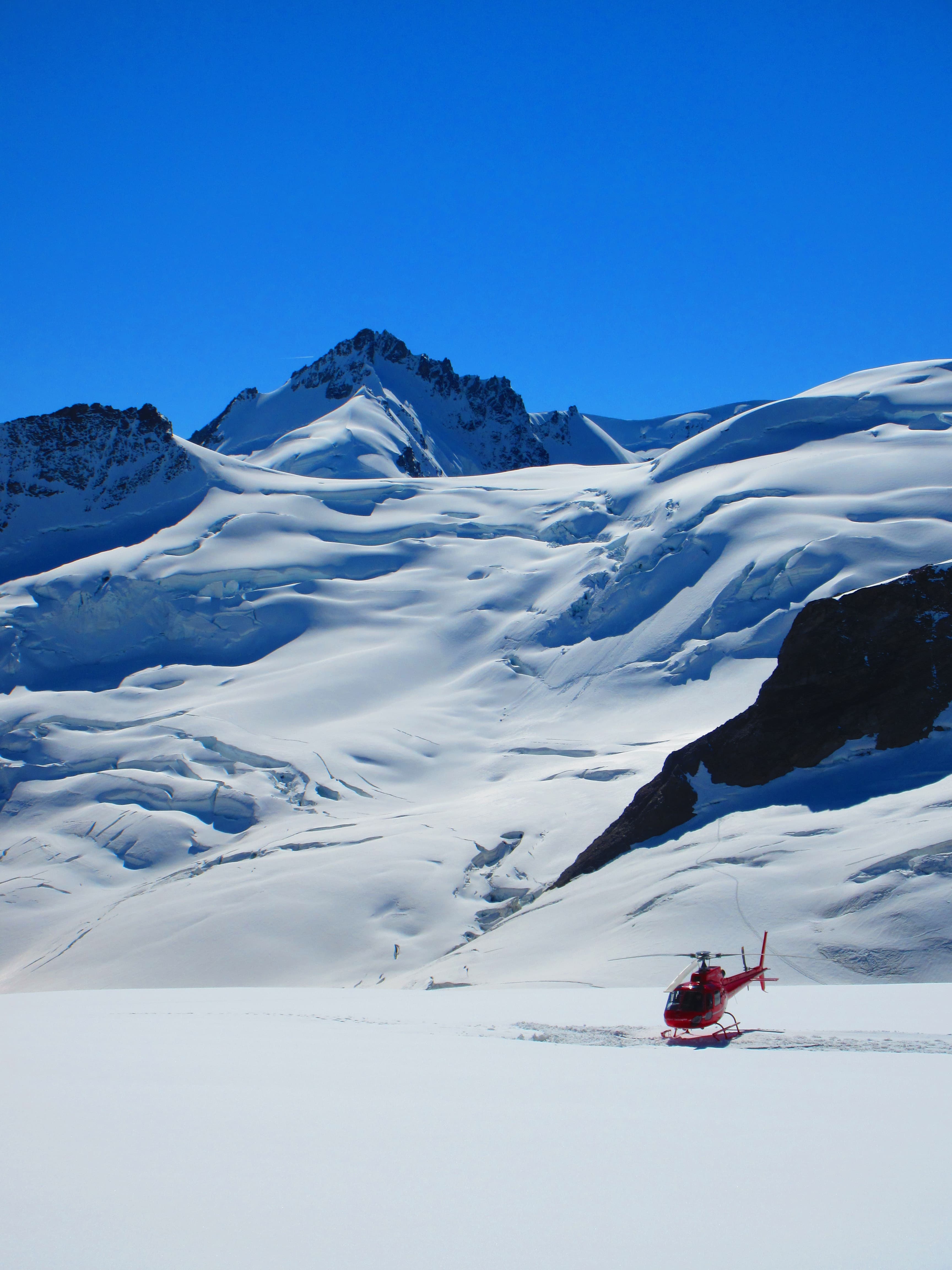 View of a helicopter landing in snow-covered mountains under clear skies