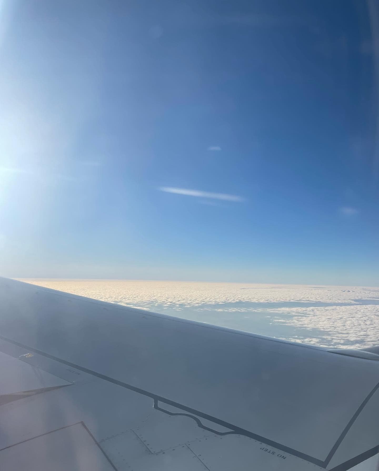View of an airplane wing and bright blue sky seen through the plane window
