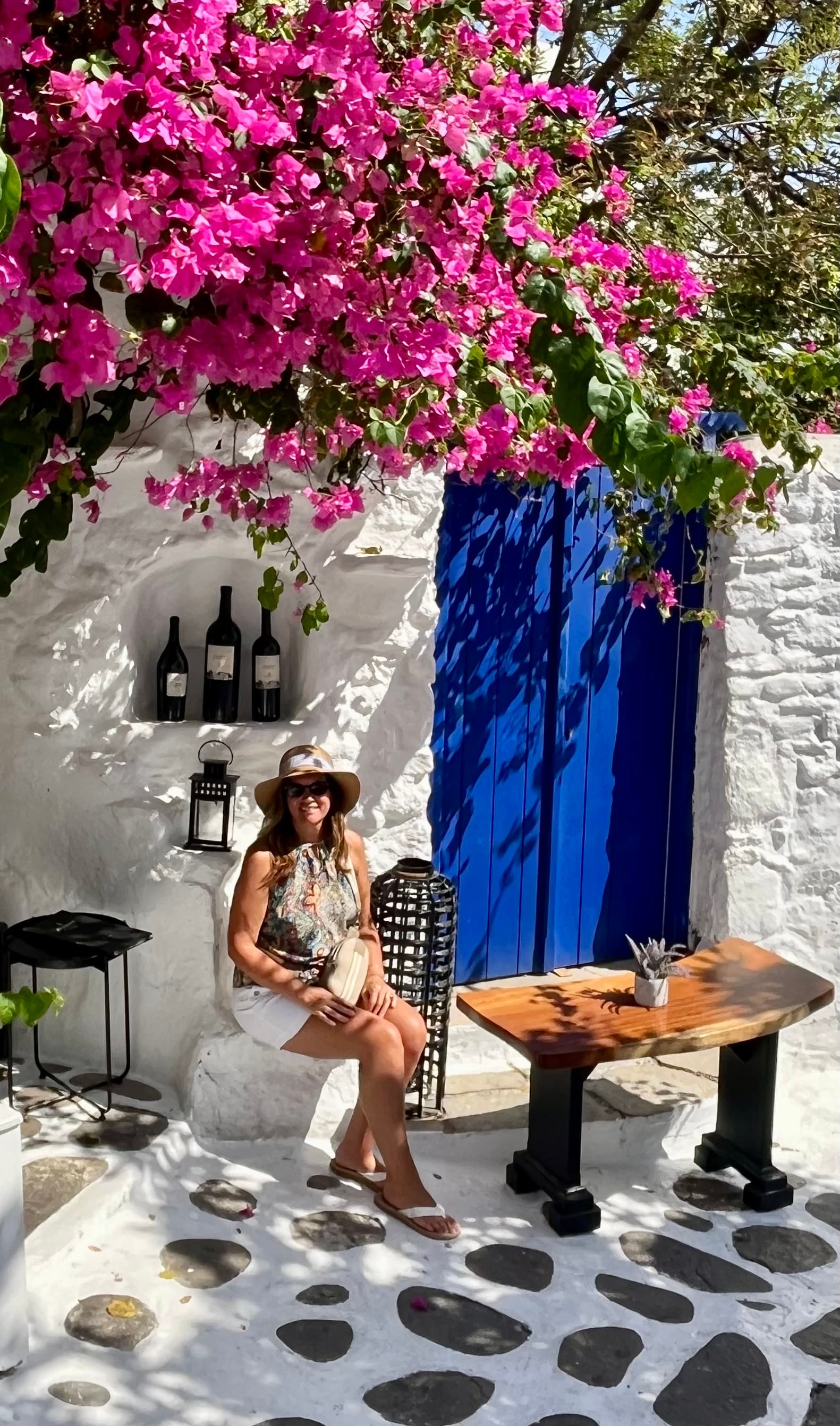 Jayme seated on a bench, with a white house and blooming pink flowers in the background.