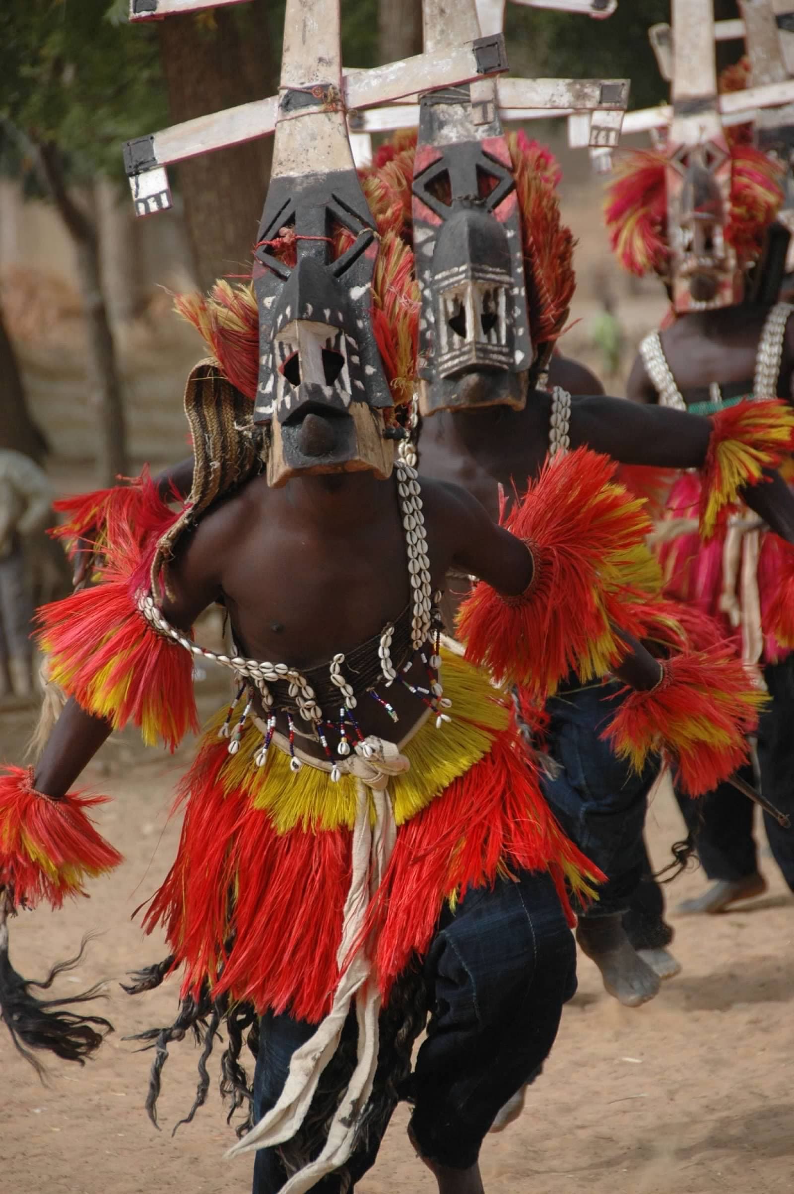 View of men running in traditional dress with elaborate masks and red skirts