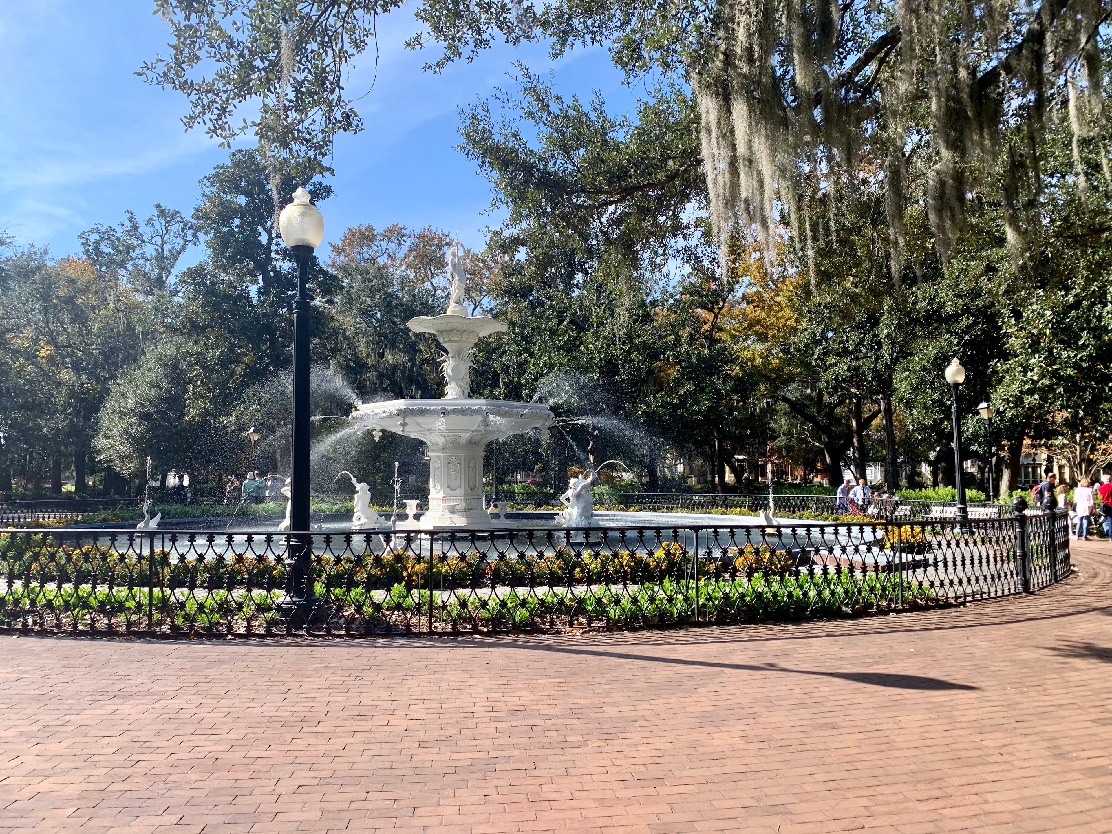 Circular white fountain in a park with trees hanging above on a sunny day