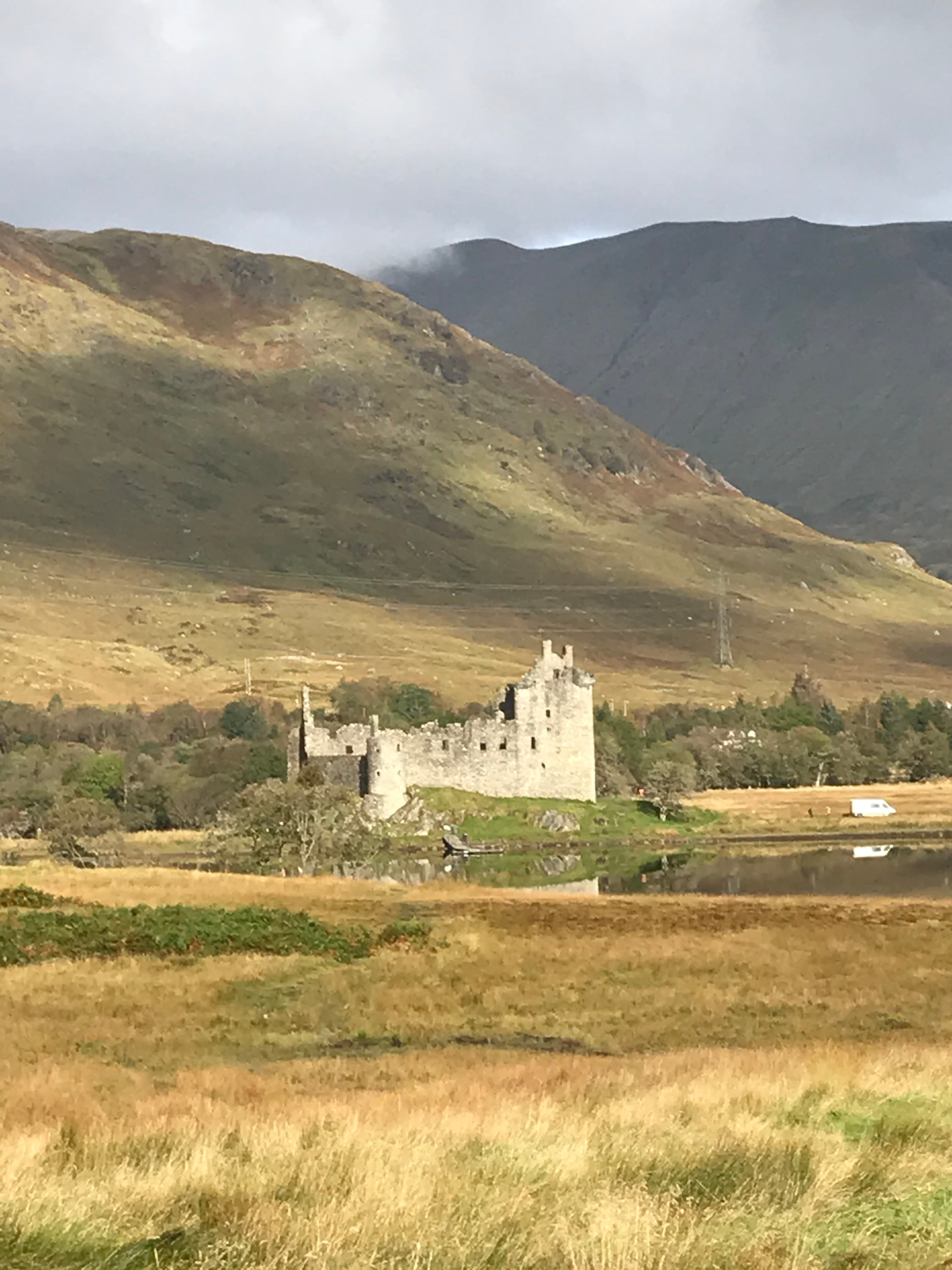 View of an old castle in the distance set amidst a green countryside with clouds in the sky